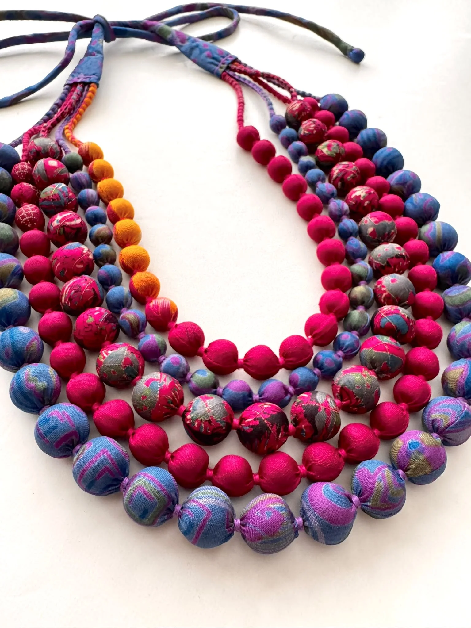 Close up of vibrant rainbow bead necklace handmade from upcycled sari silk in shades of yellow, pink, olive and blue