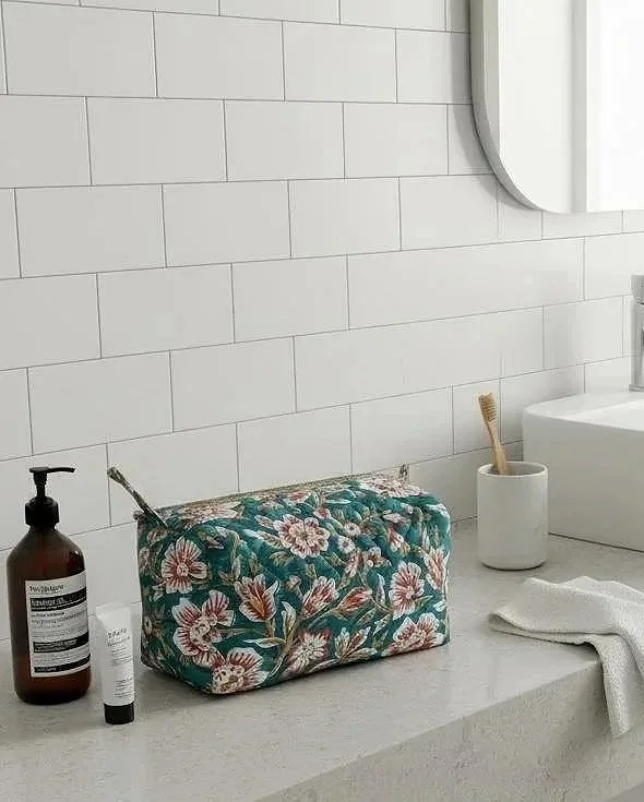 Colourful quilted cotton toiletries bag hand block printed in a teal, white and red floral design, resting on a modern white bathroom counter.
