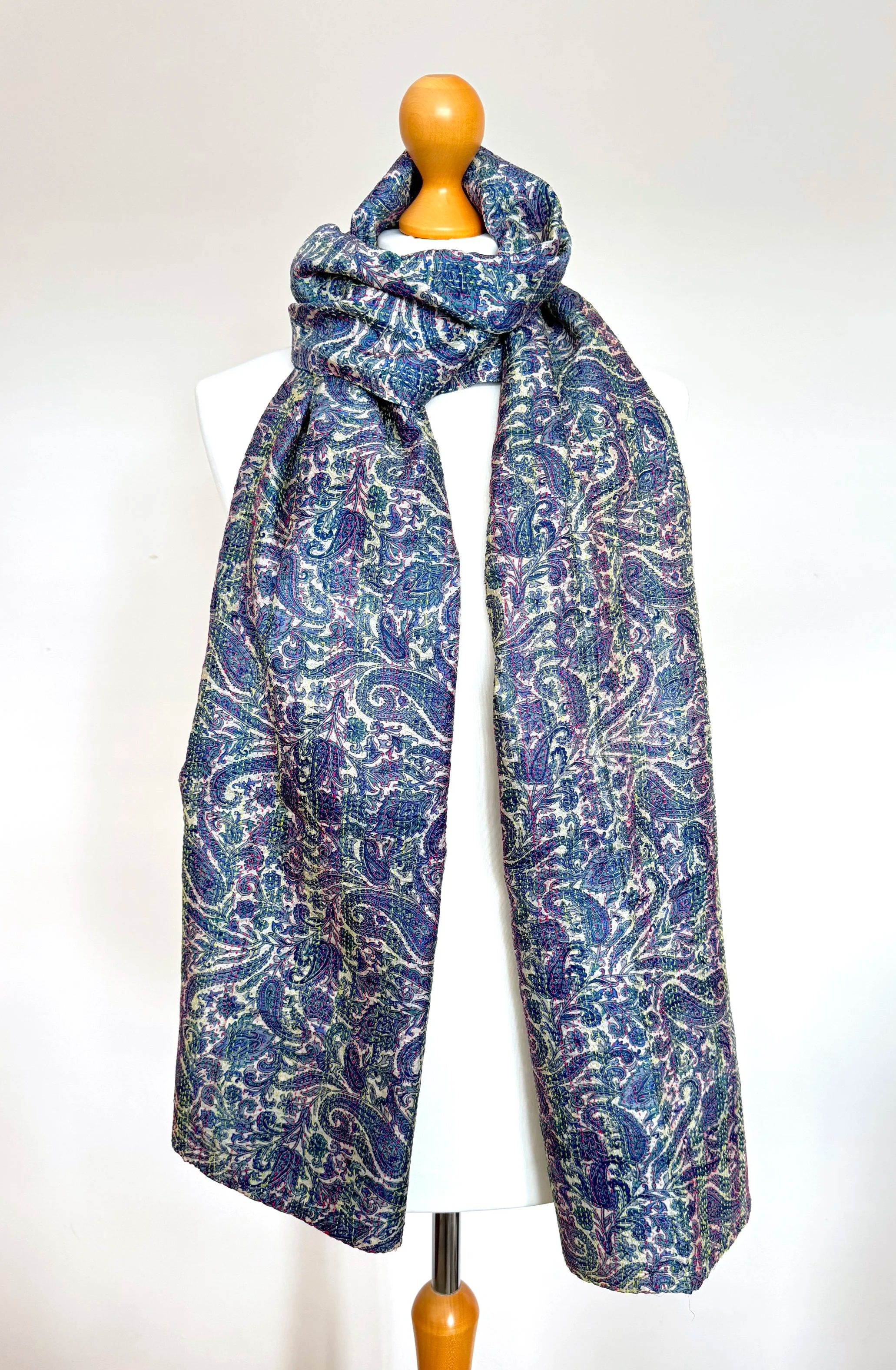 Elegant blue paisley patterned scarf draped over a white mannequin with a wooden stand, against a simple white background.