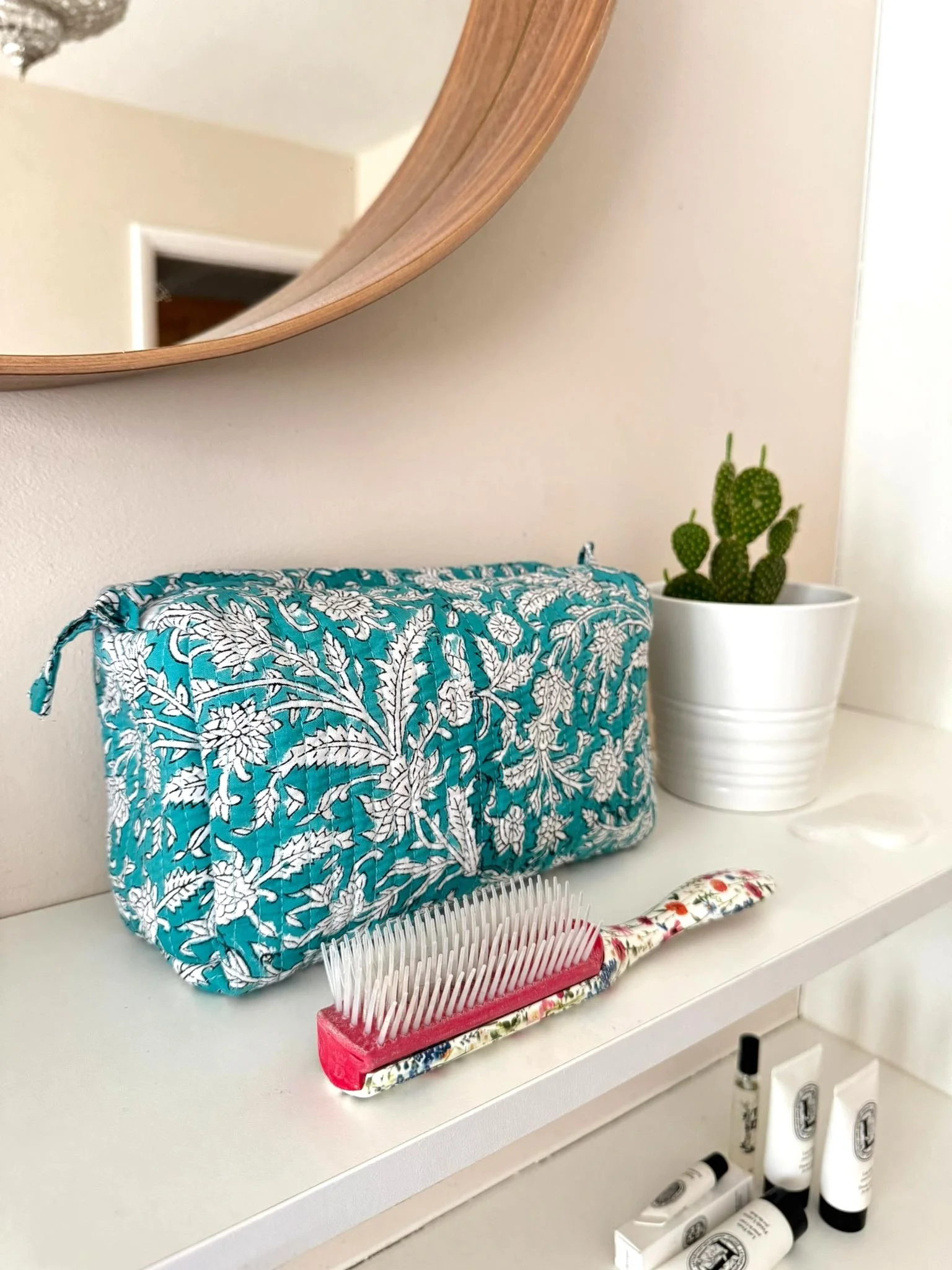 Hand block printed toiletry travel pouch resting on a bedroom shelf under a mirror, there is a hair brush resting in front of it