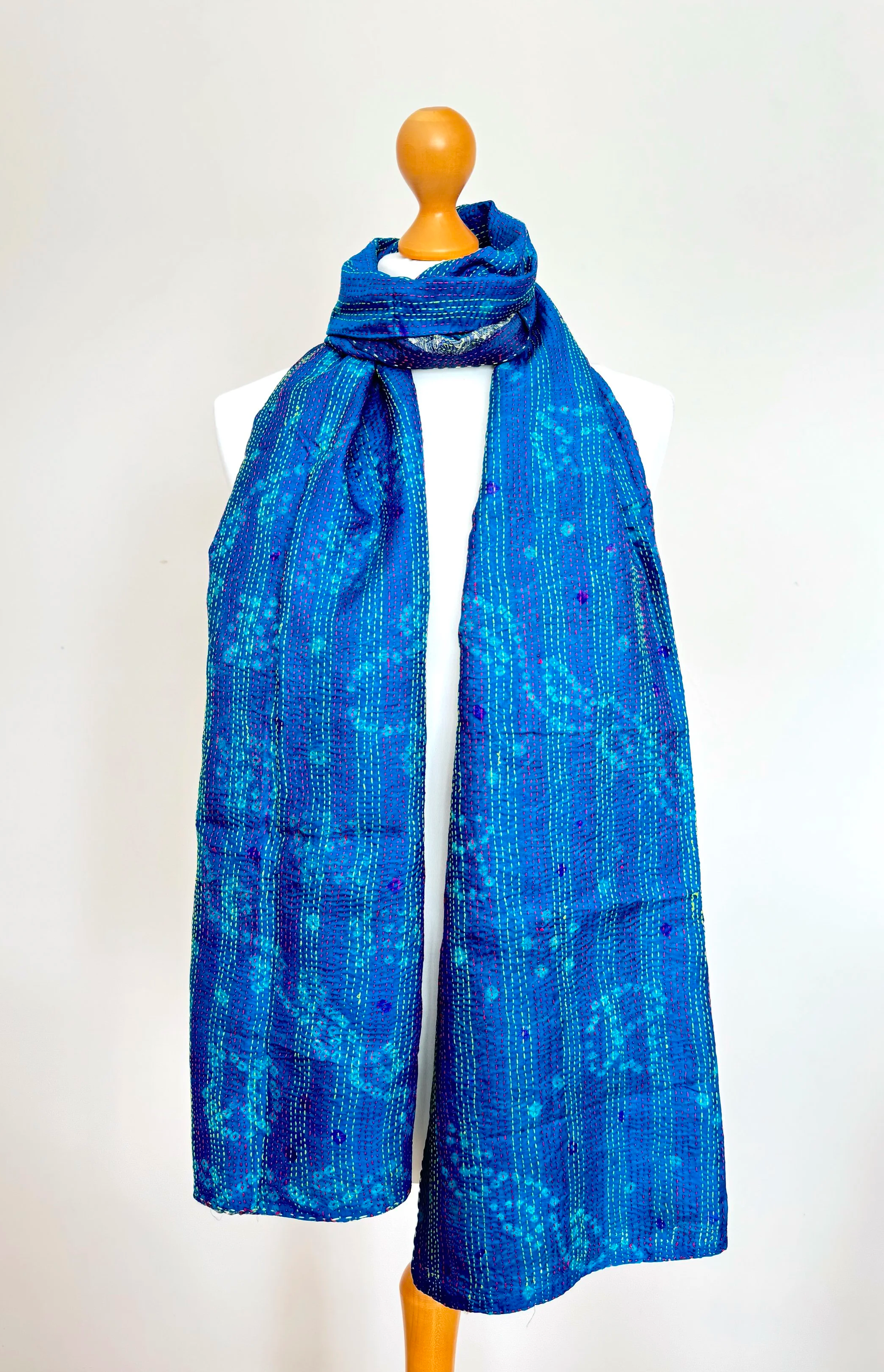 A vibrant blue scarf with intricate patterns is elegantly draped around a neutral-colored mannequin against a plain white background.
