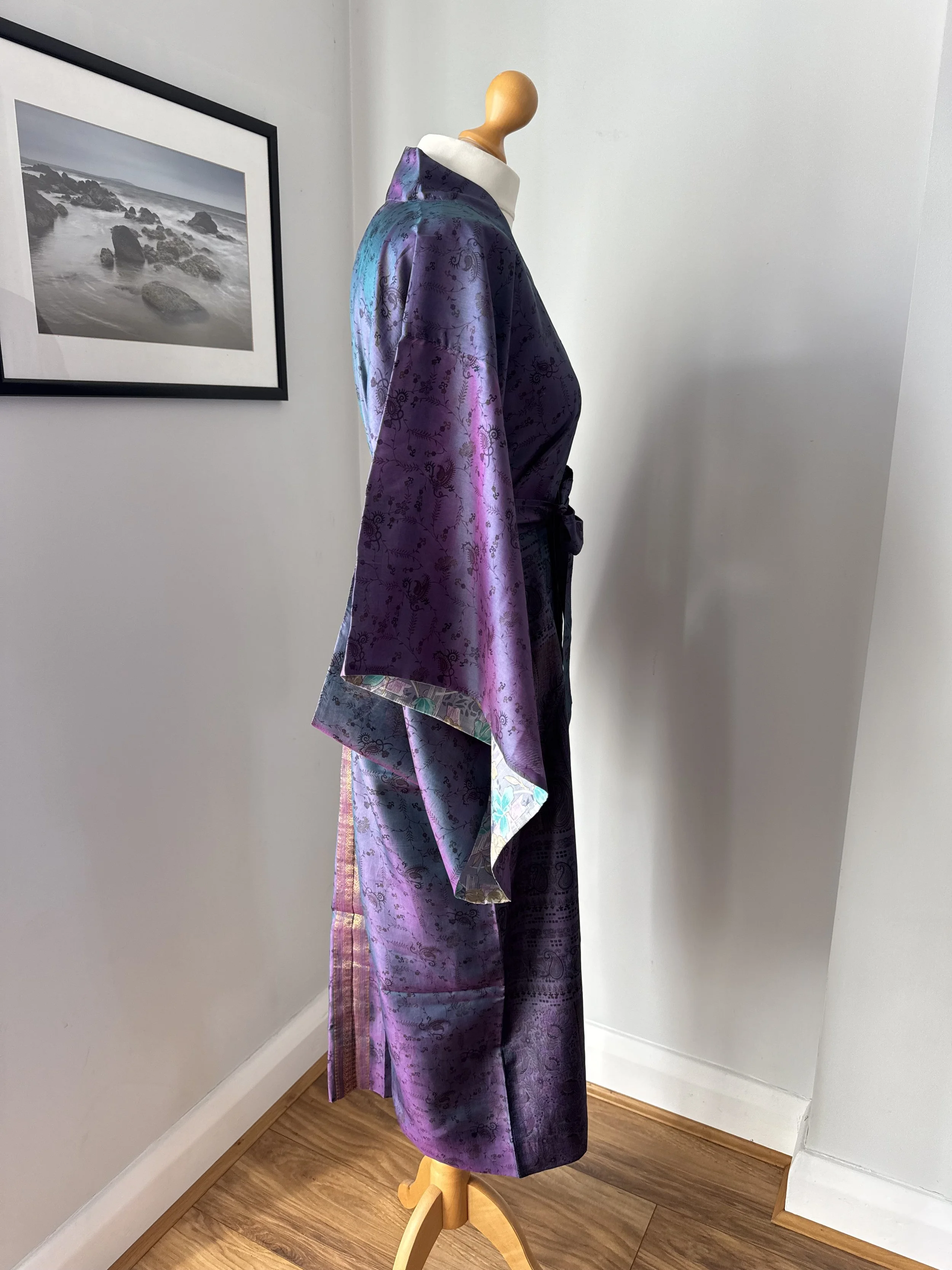 Side view of long silk kimono cover up in purple with wrap-over design, flowing kimono sleeves and silk tie belt against a grey wall