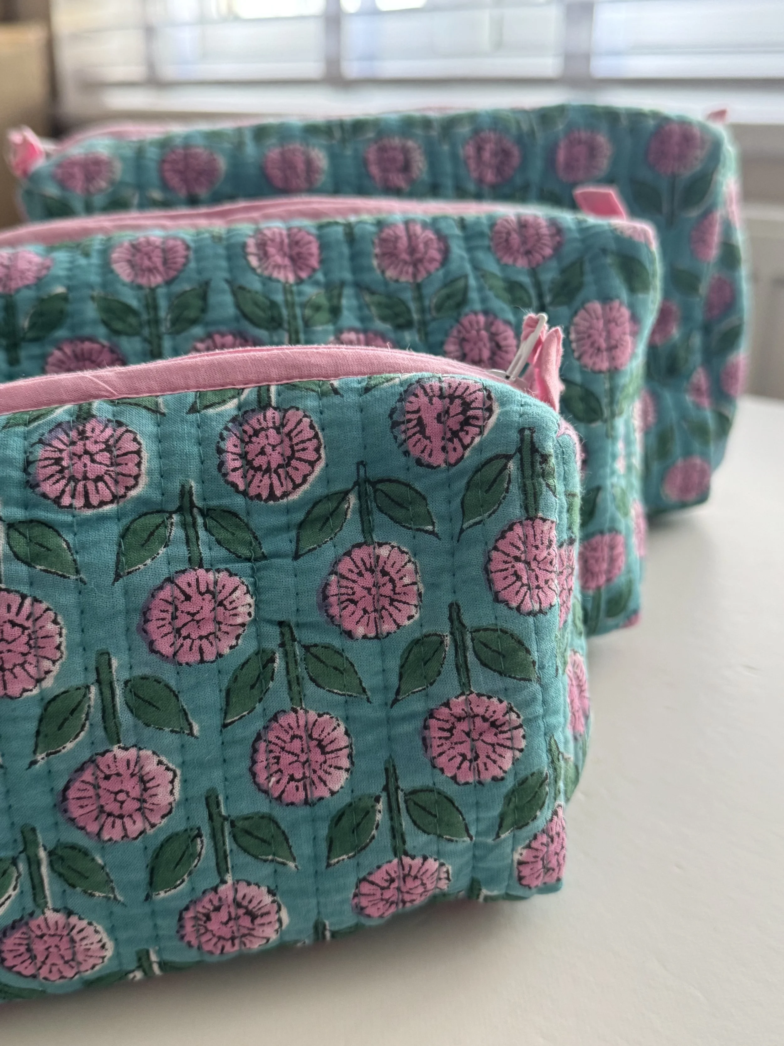 Close up of set of three block print quilted cotton wash bags with pink flowers on a blue fabric.