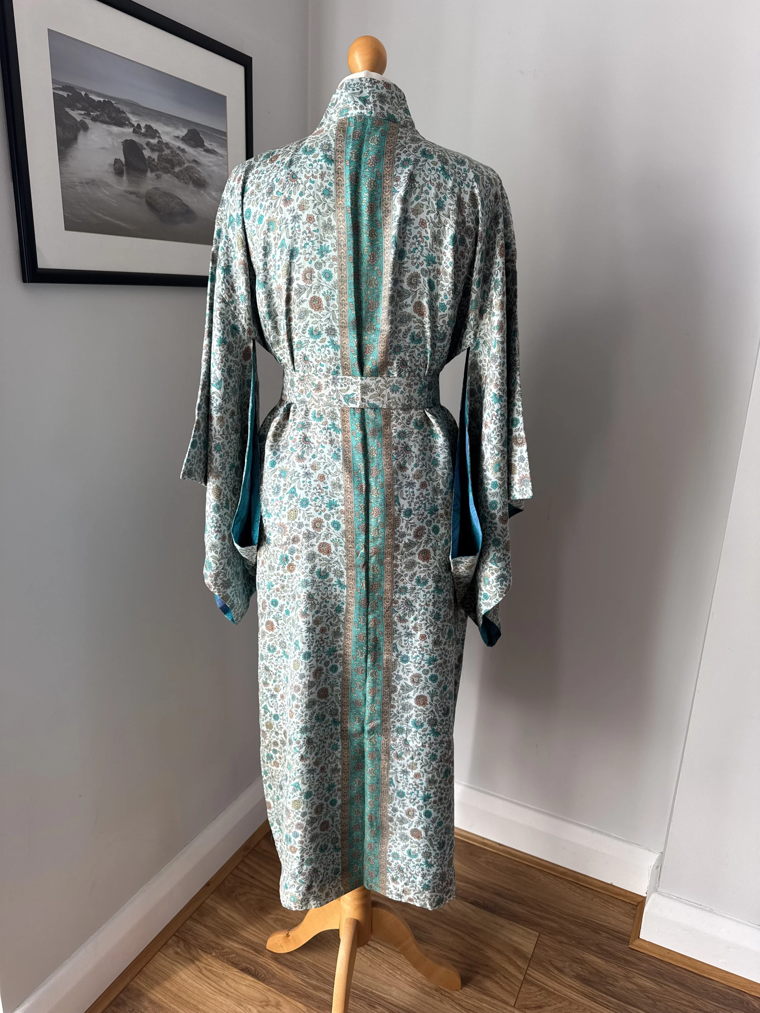 Back view of floral silk kimono dressing robe with turquoise and cinnamon flowers, turquoise strip running down the back and flowing kimono sleeves.