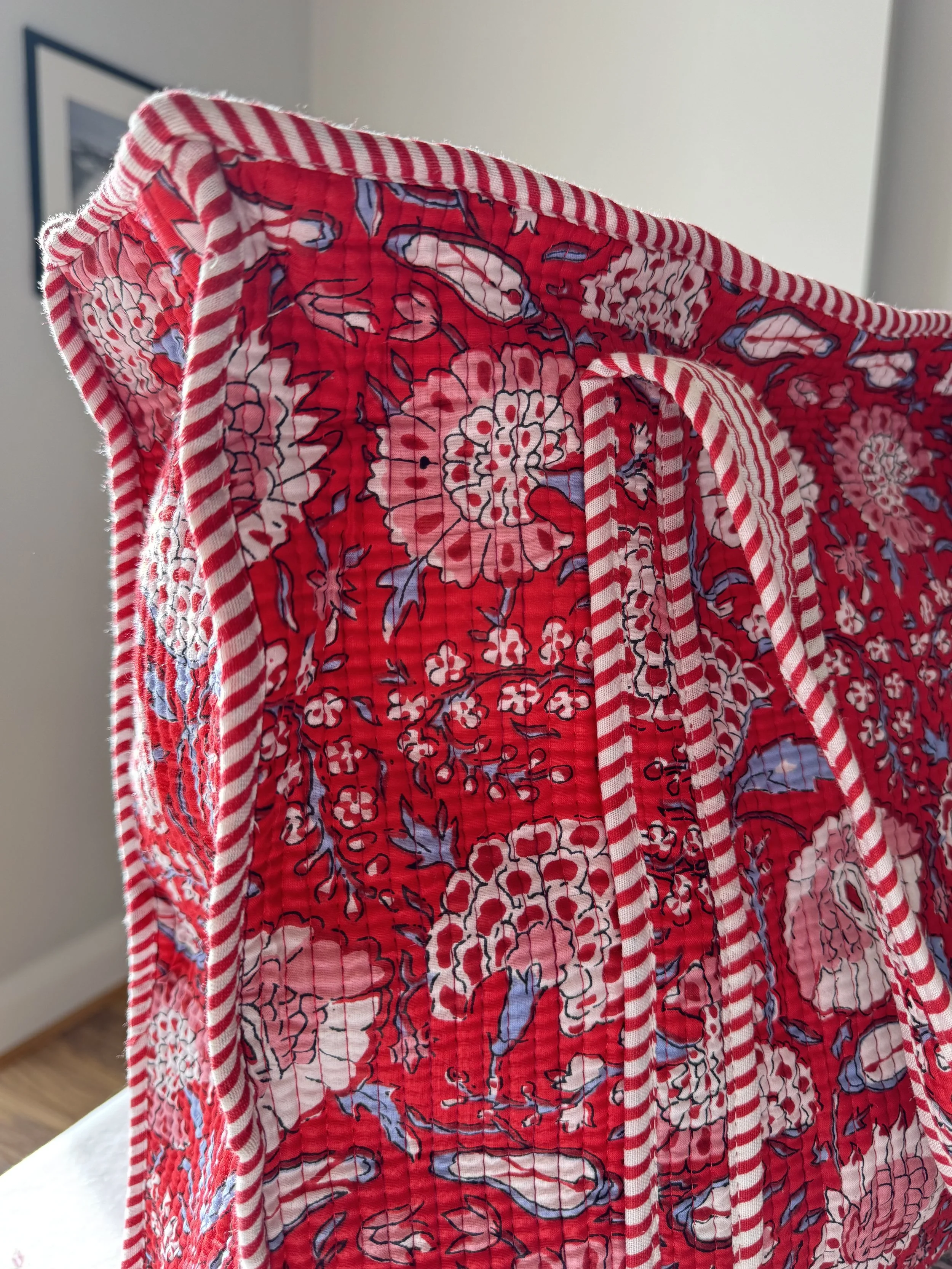 Close up of vibrant red floral quilted tote bag with striped straps and trims