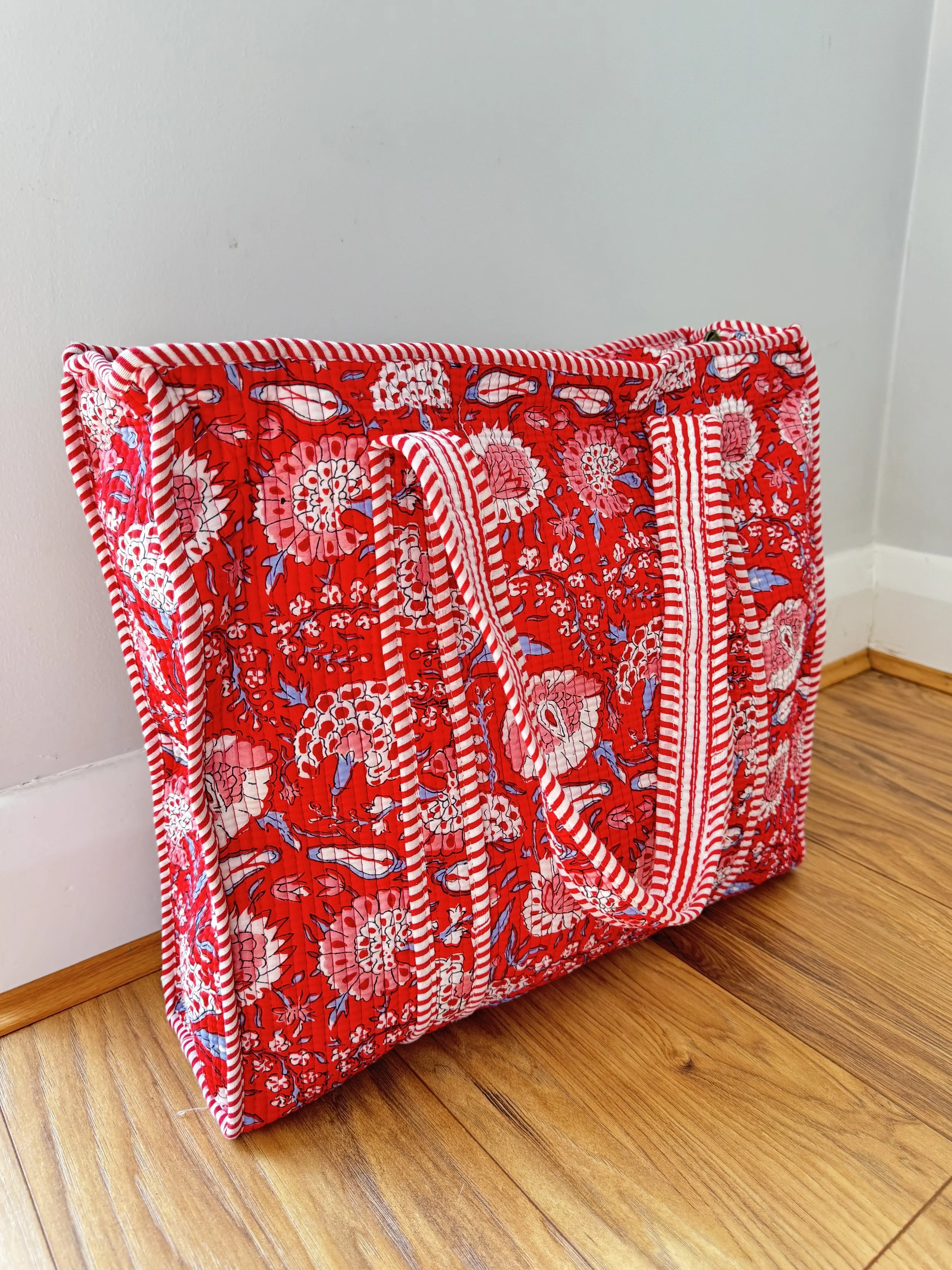 Screen printed quilted cotton tote bag in bold red and white floral pattern by Jewelled Buddha, placed on a wooden floor with a neutral background