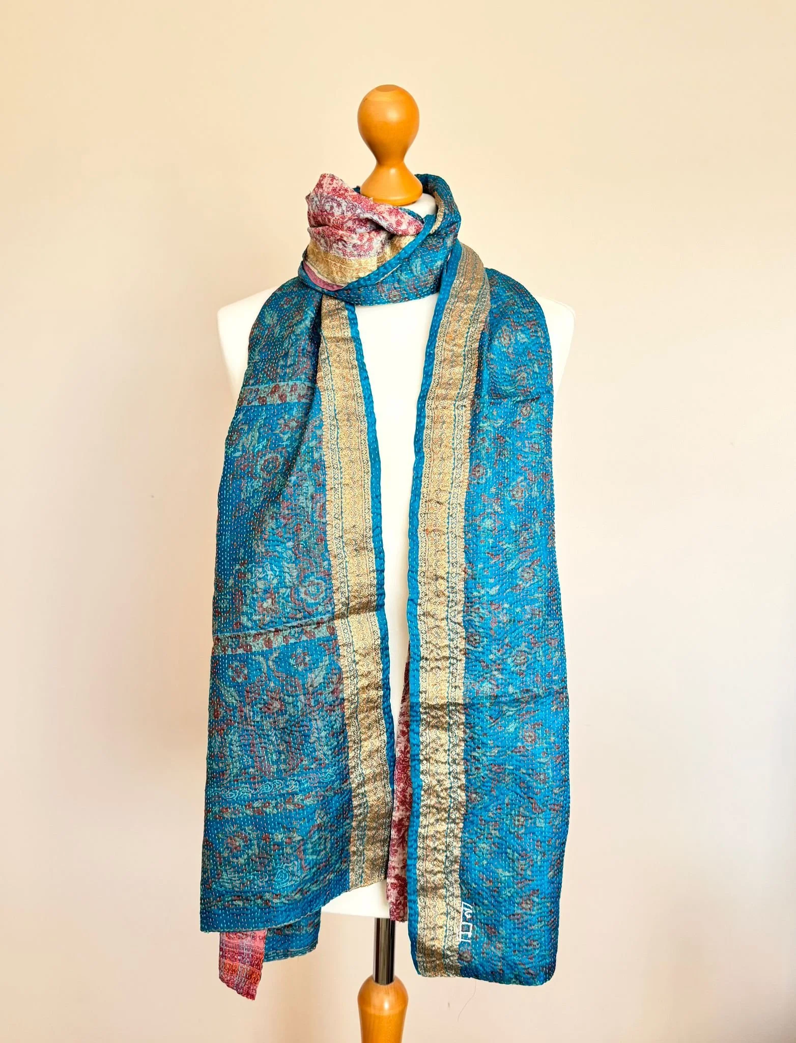 A blue and gold patterned silk scarf draped elegantly over a mannequin against a peach background