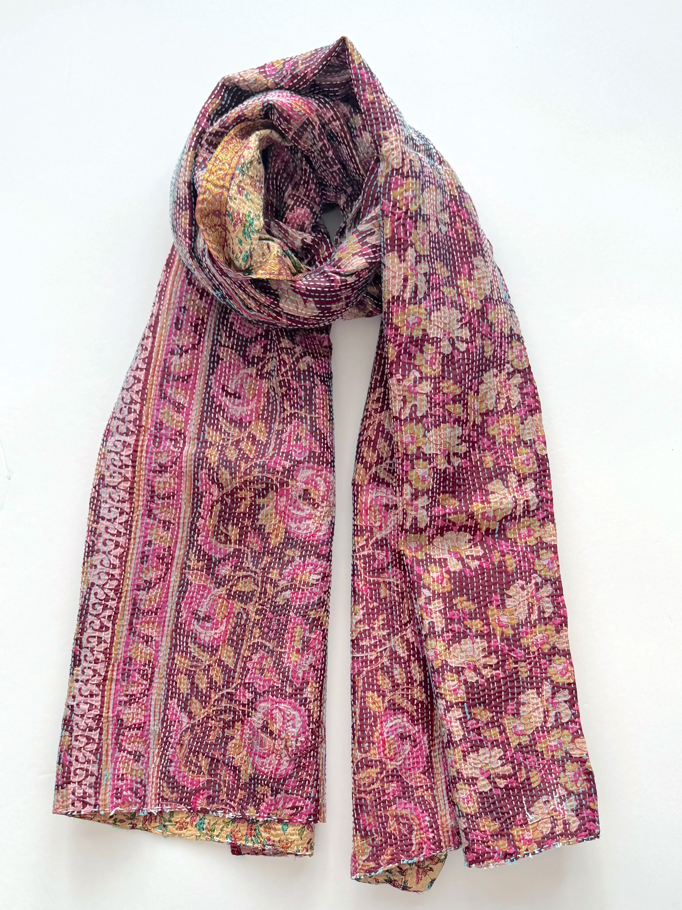 A richly patterned scarf with vibrant pink, maroon, and beige floral designs, draped elegantly on a white background, conveys warmth and elegance.