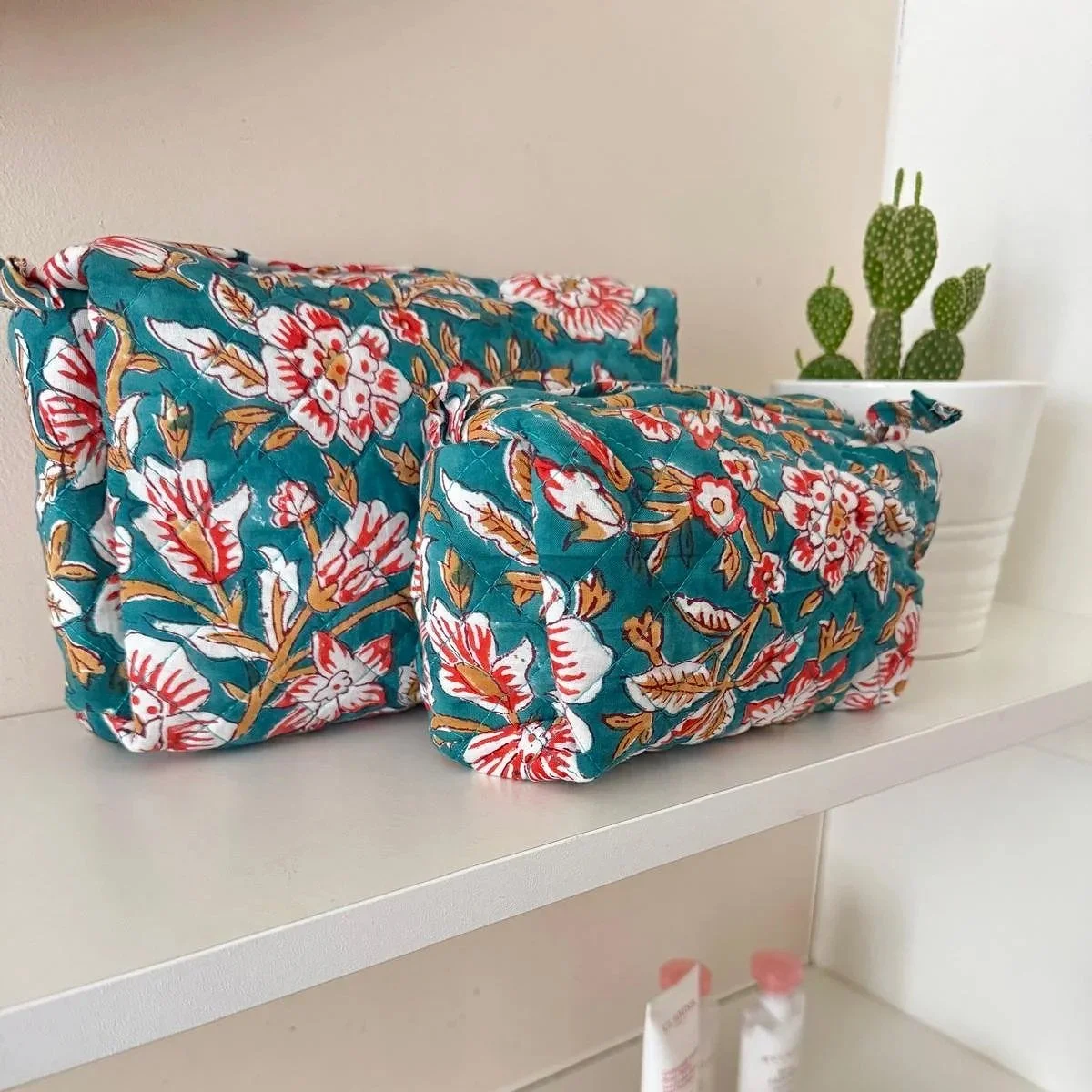 Two handmade cosmetic pouches resting on a white shelf with toiletries resting on the shelf below