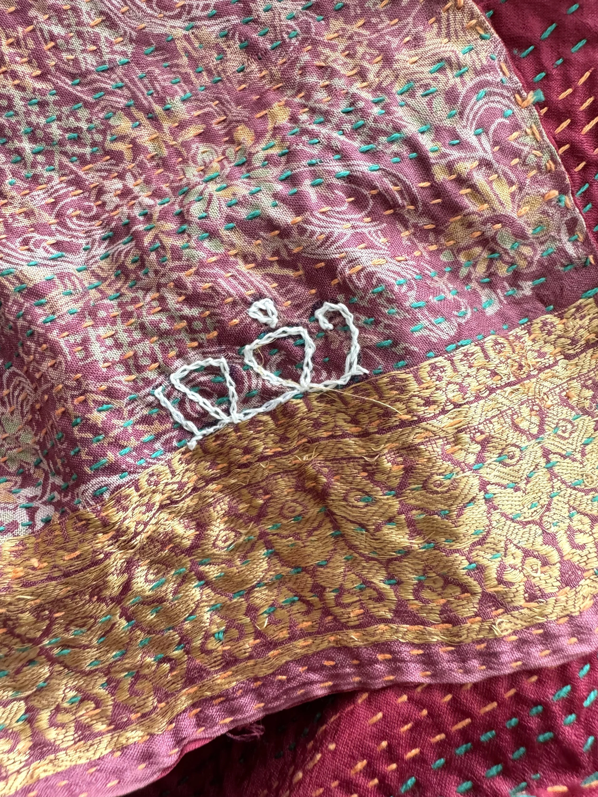 Richly patterned textile with intricate gold embroidery and teal stitching on a deep red background.