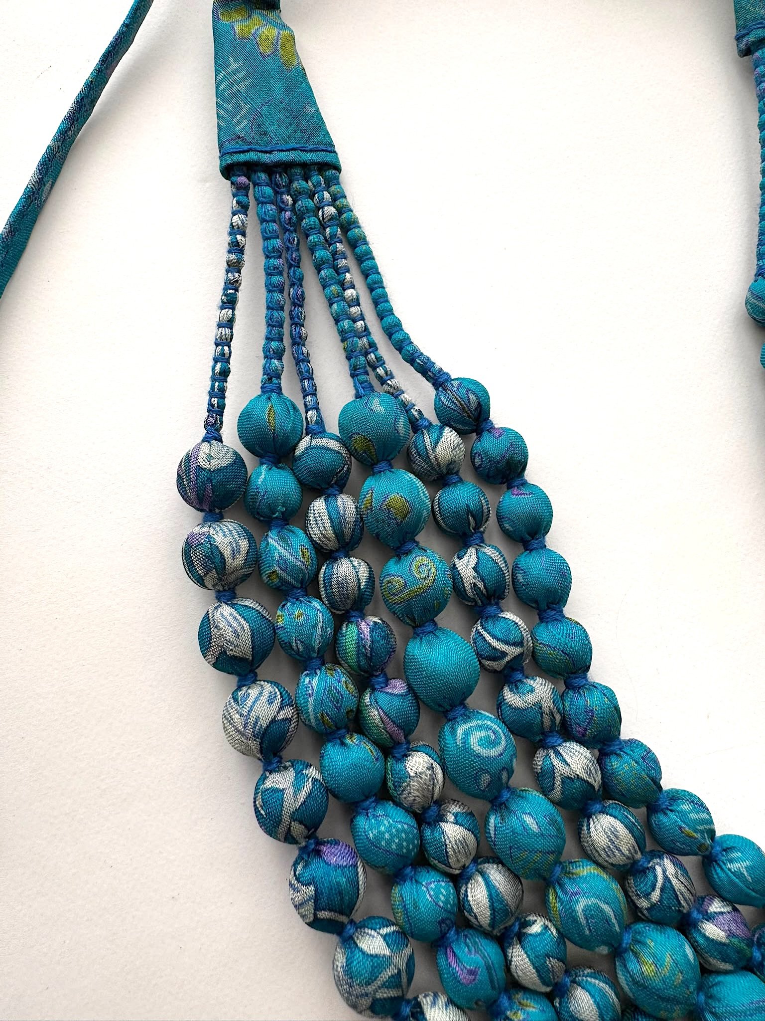 Close up of vintage sari blue beaded necklace on a white background.