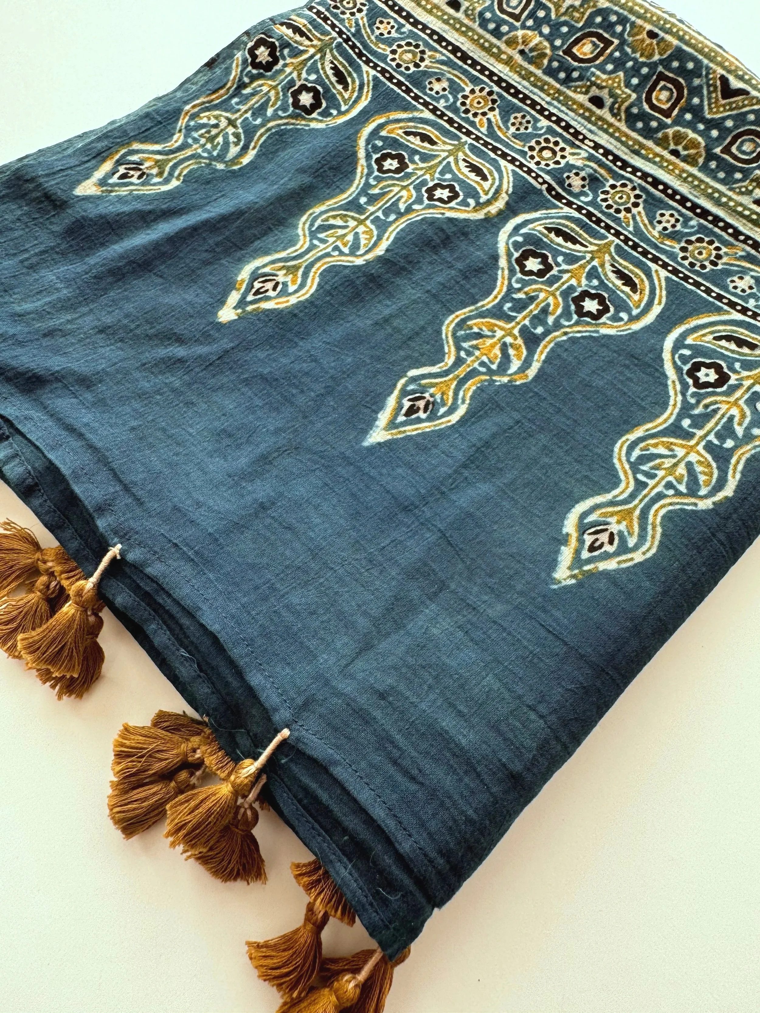 Folded indigo and olive Ajrakh scarf showing the tassel edge and block printed border
