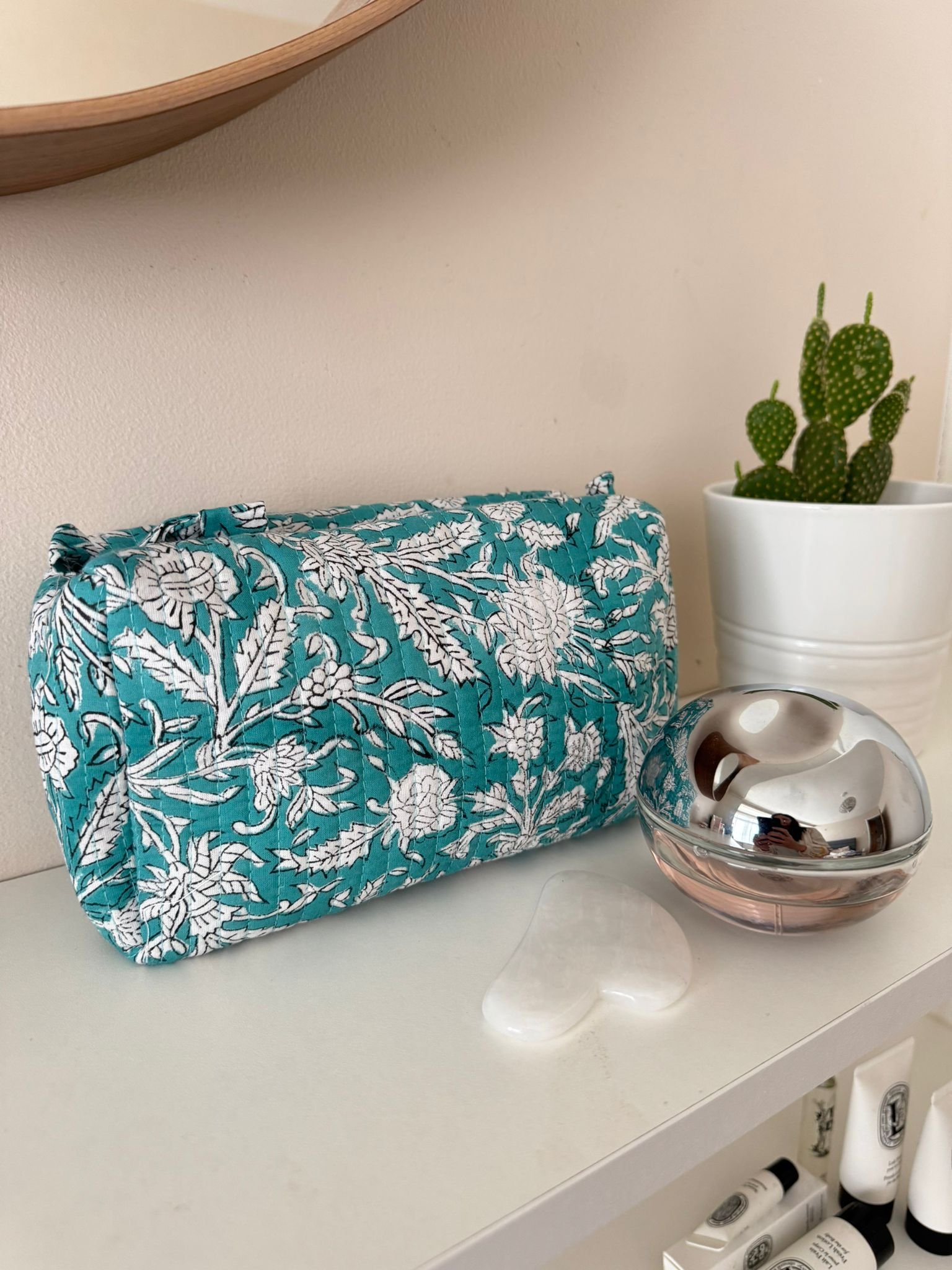 Hand block printed toiletry travel pouch resting on a bedroom shelf with a leafy botanical print in white