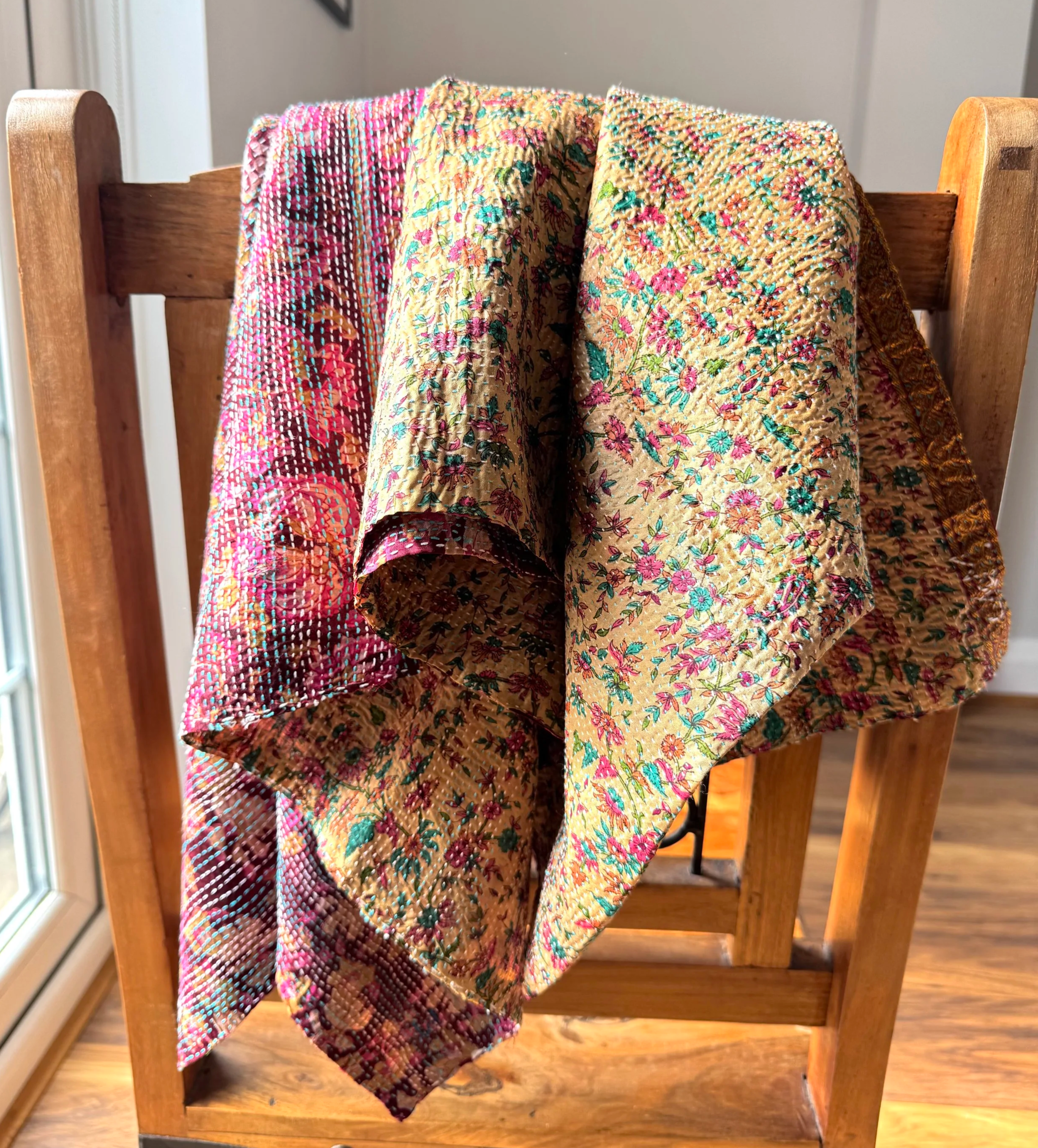 Colourful, intricately patterned vintage sari silk scarf wrap draped over a wooden chair, illuminated by natural light from a nearby window