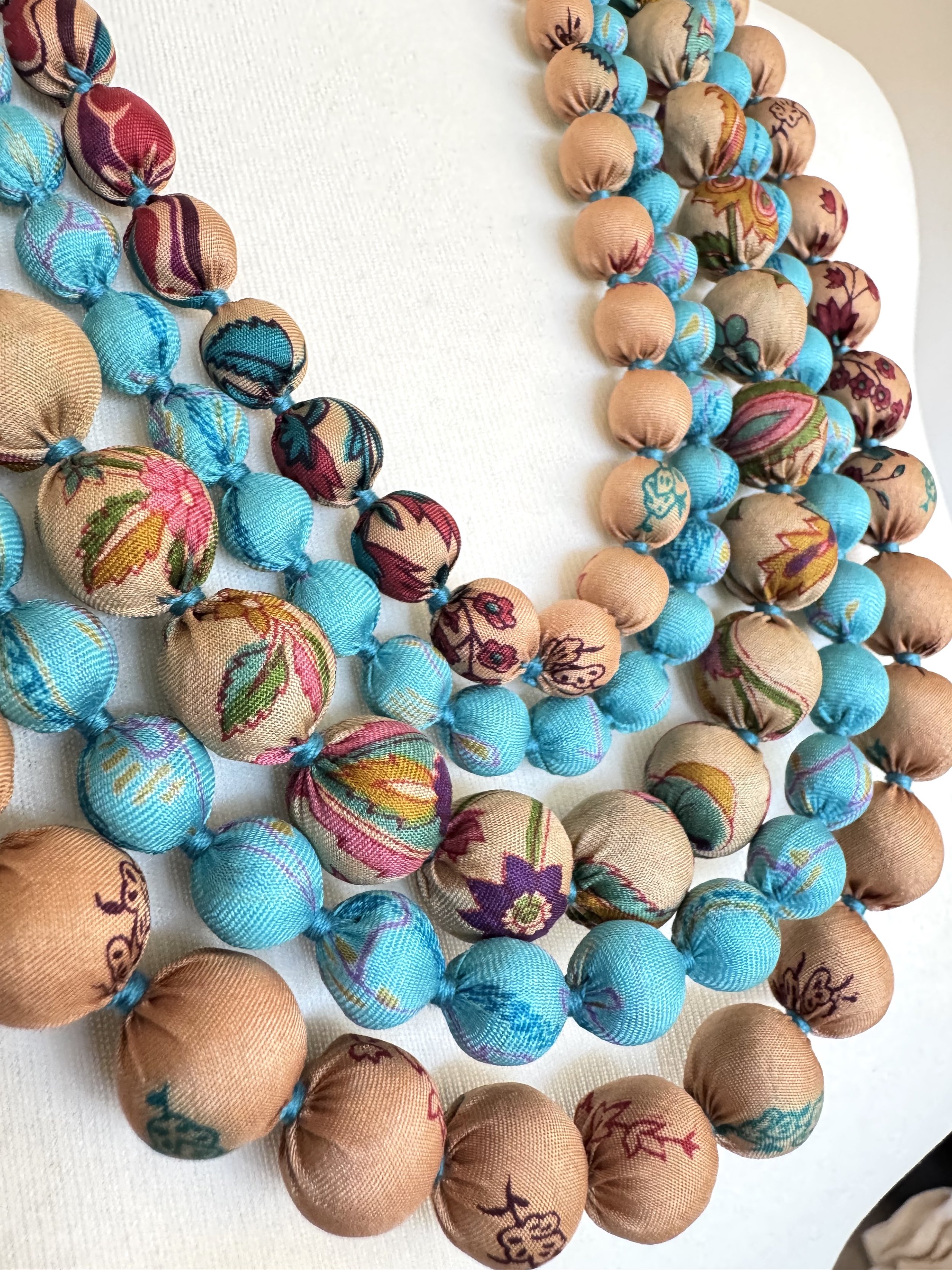 Handmade five-strand necklace featuring upcycled wooden prayer beads wrapped in recycled sari silk in multicolour shades, layered elegantly on a white mannequin..
