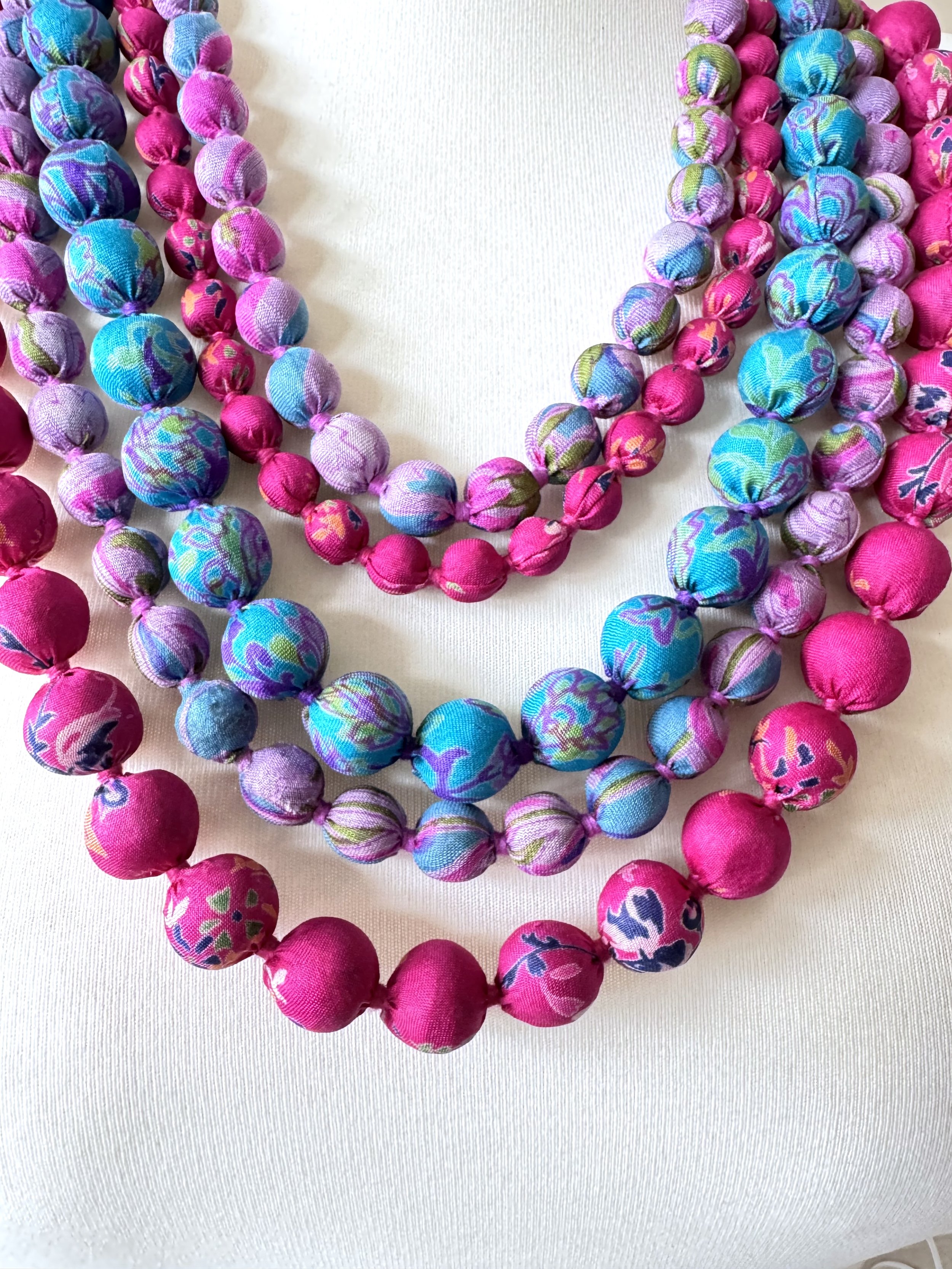 Close up of colourful beaded necklace featuring upcycled wooden beads wrapped in recycled sari silk, layered elegantly on a white mannequin.