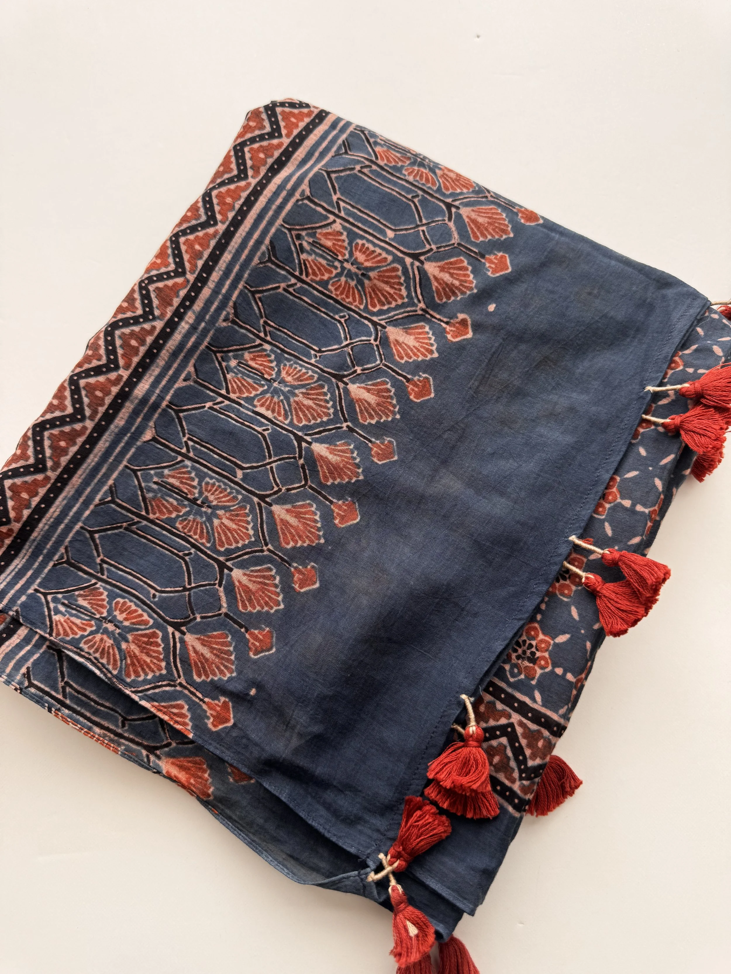Folded indigo and rust red Ajrakh scarf showing the block printed border and tassel edge