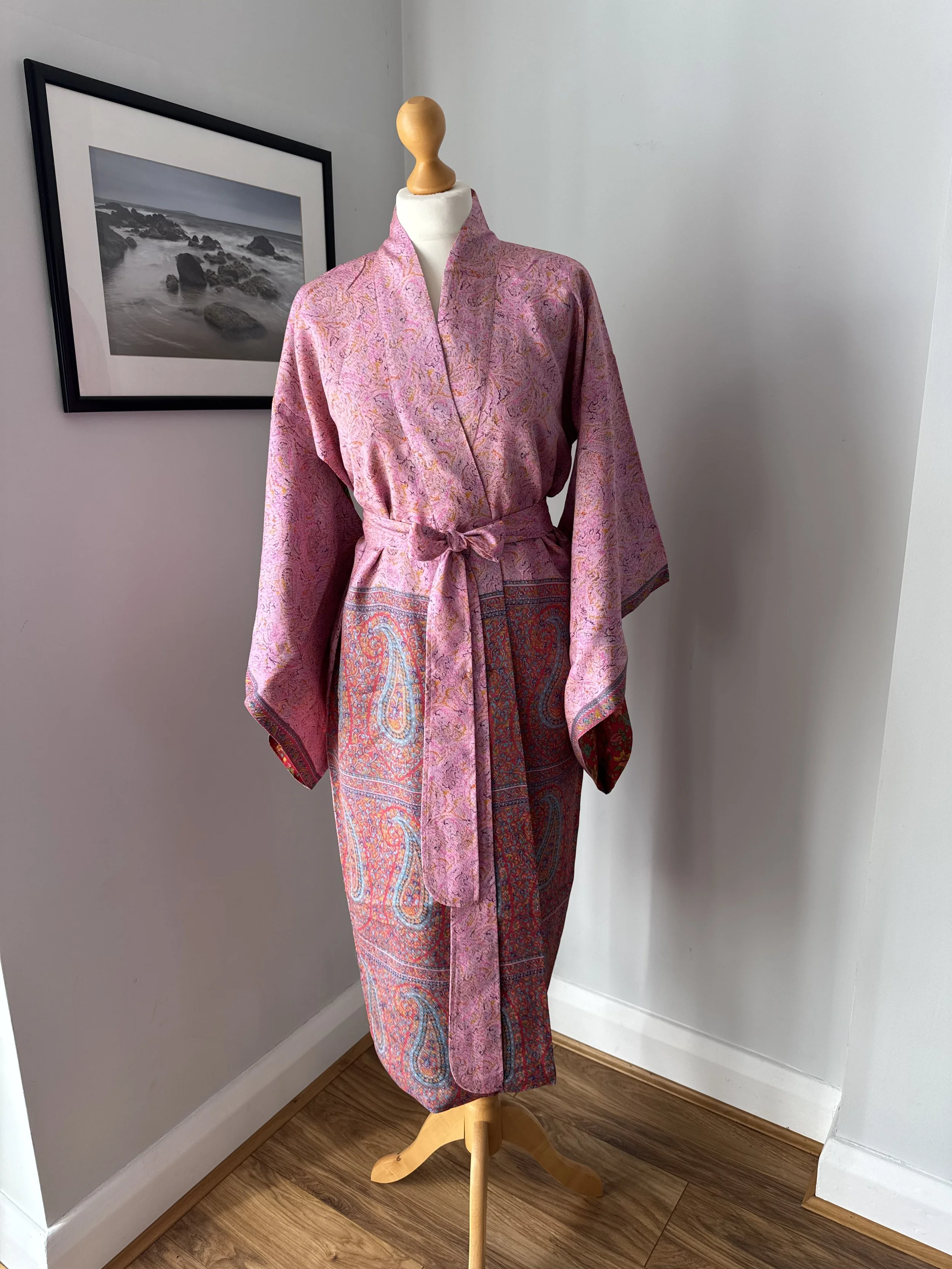Pink silk kimono robe in a soft pink with striking Paisley border, flowing kimono sleeves and silk tie belt displayed on a mannequin.