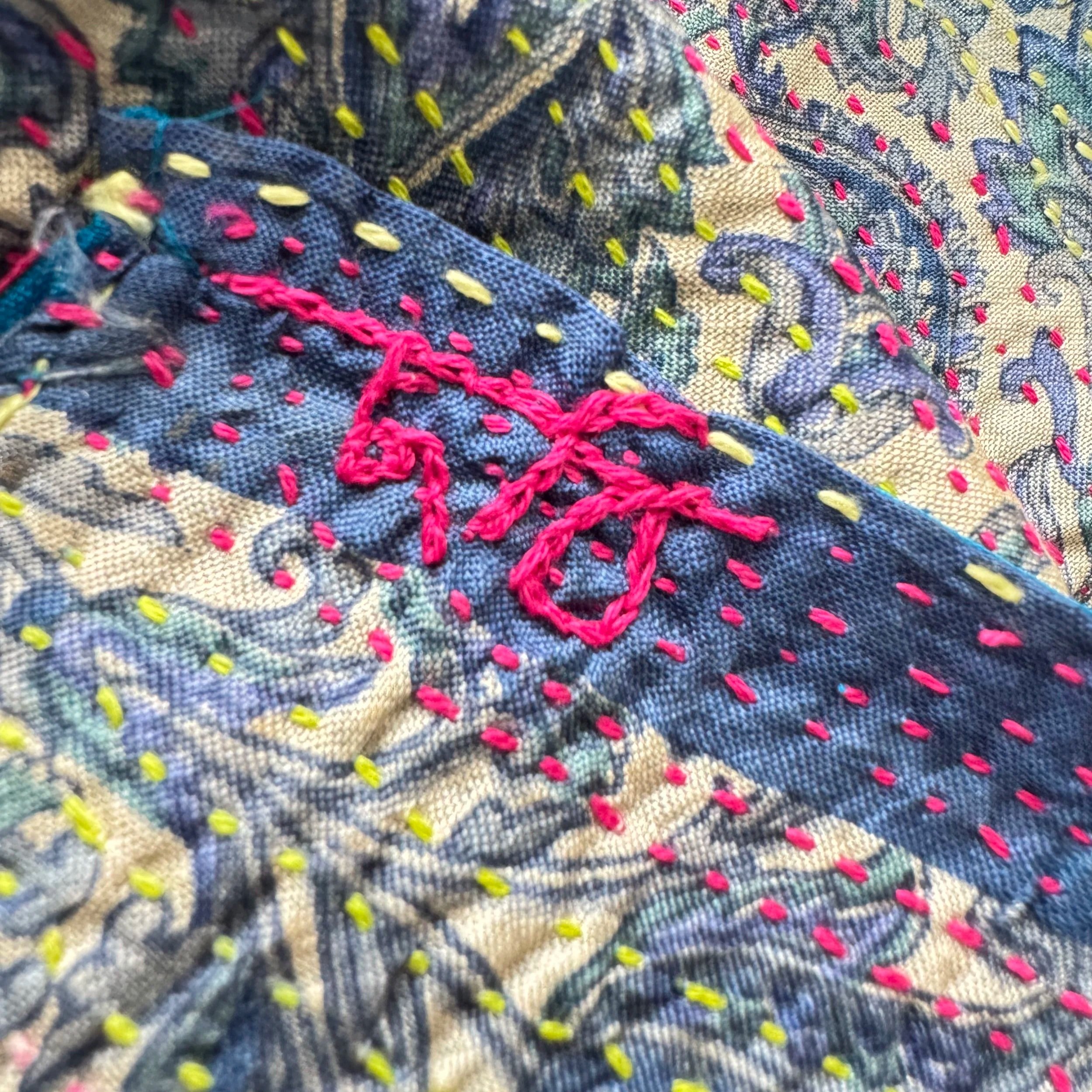 Close-up of colorful embroidery on fabric featuring intricate patterns. Pink thread stitches form abstract shapes, adding a vibrant, textured appearance.