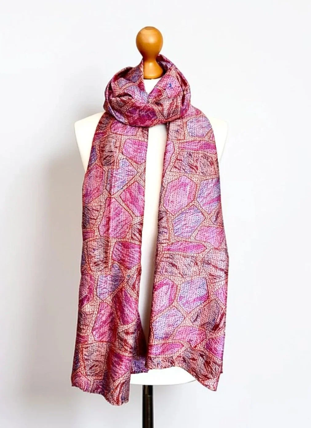 A long silky pink scarf draped around a mannequin against a white backdrop. The scarf has an abstract print with a textured look created by kantha running stitch.