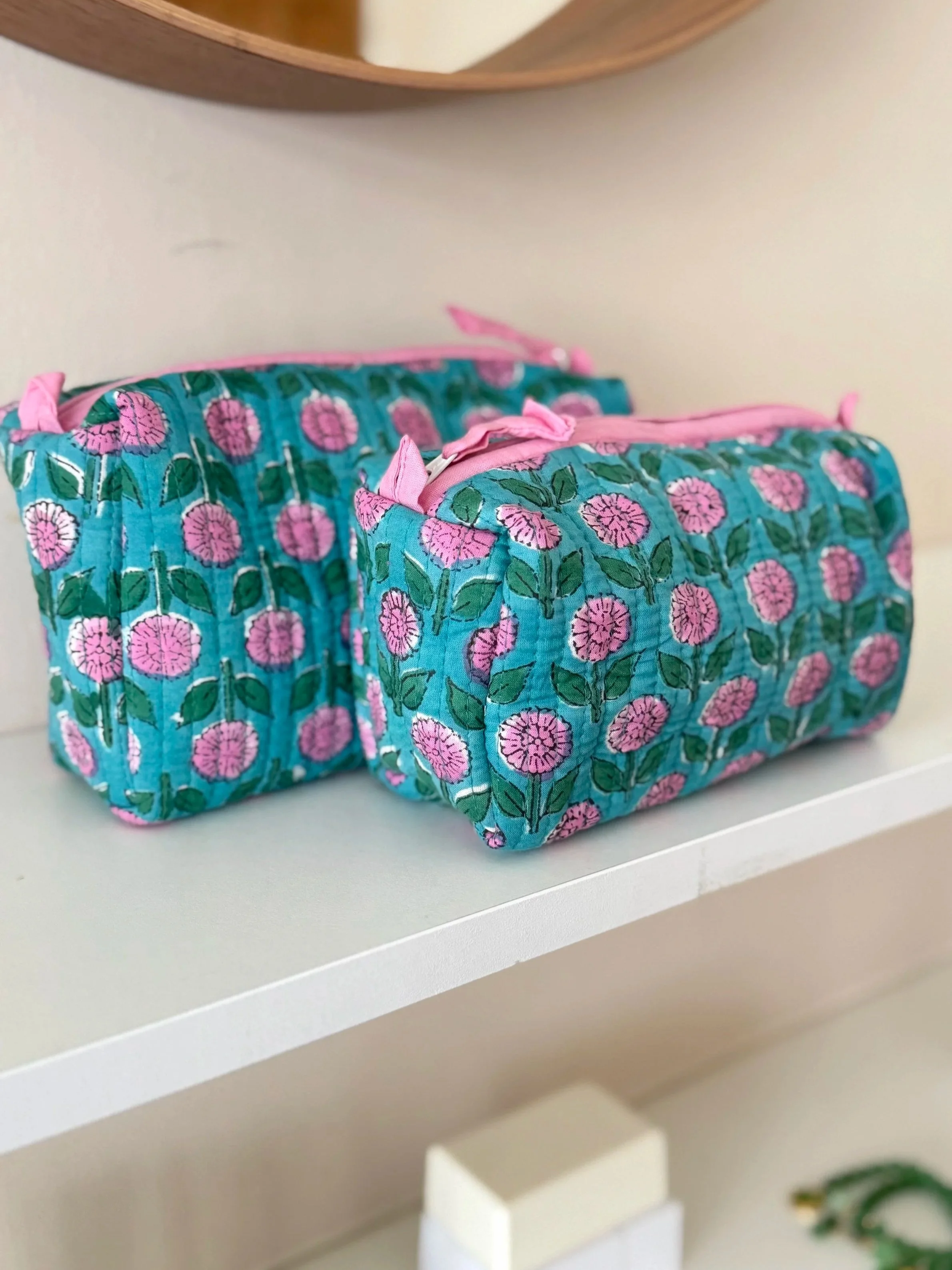 Two blue and pink floral block print cosmetic bags resting on a white shelf