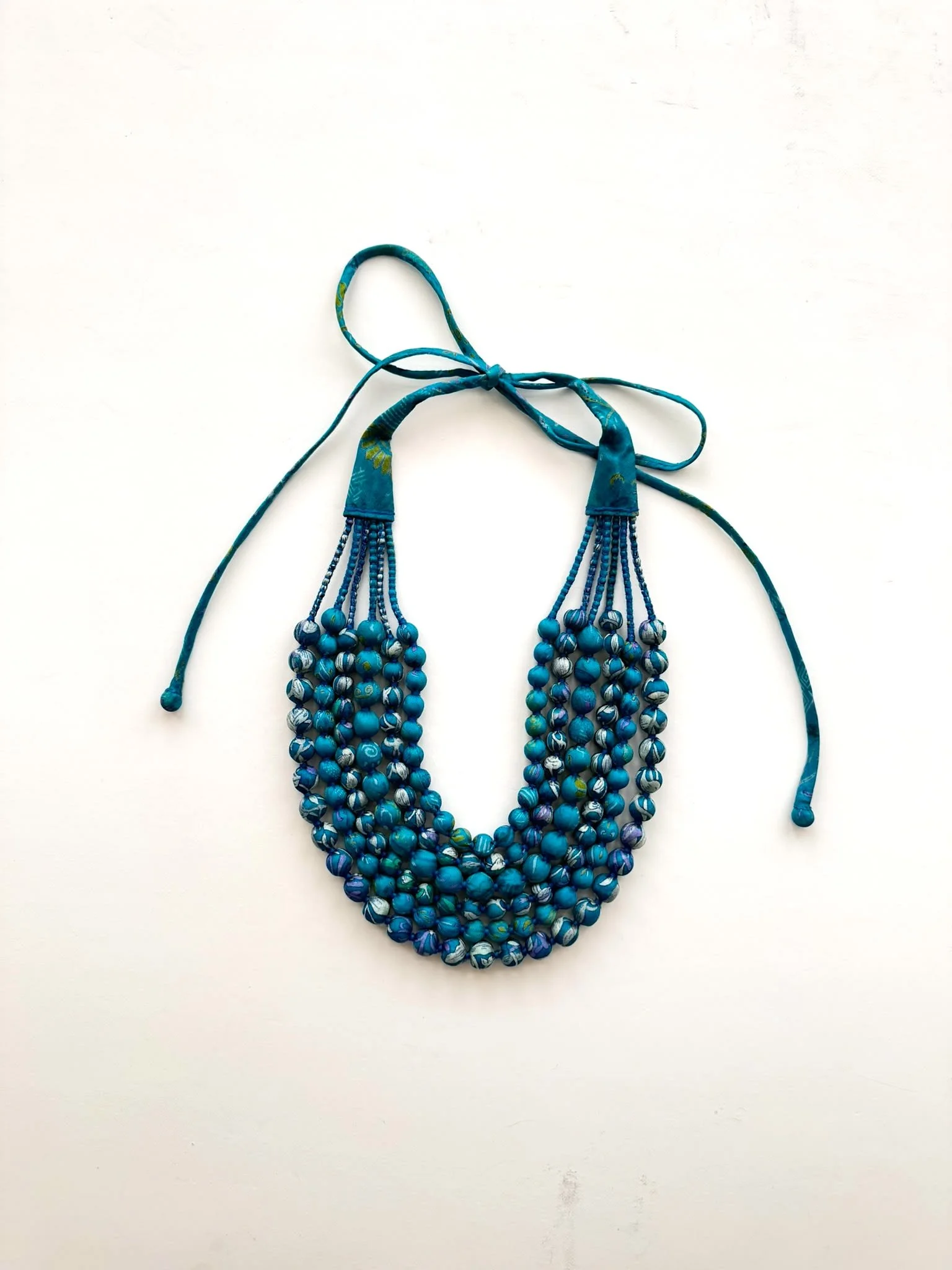Multi-layered blue bead necklace with adjustable tie-back against a white background
