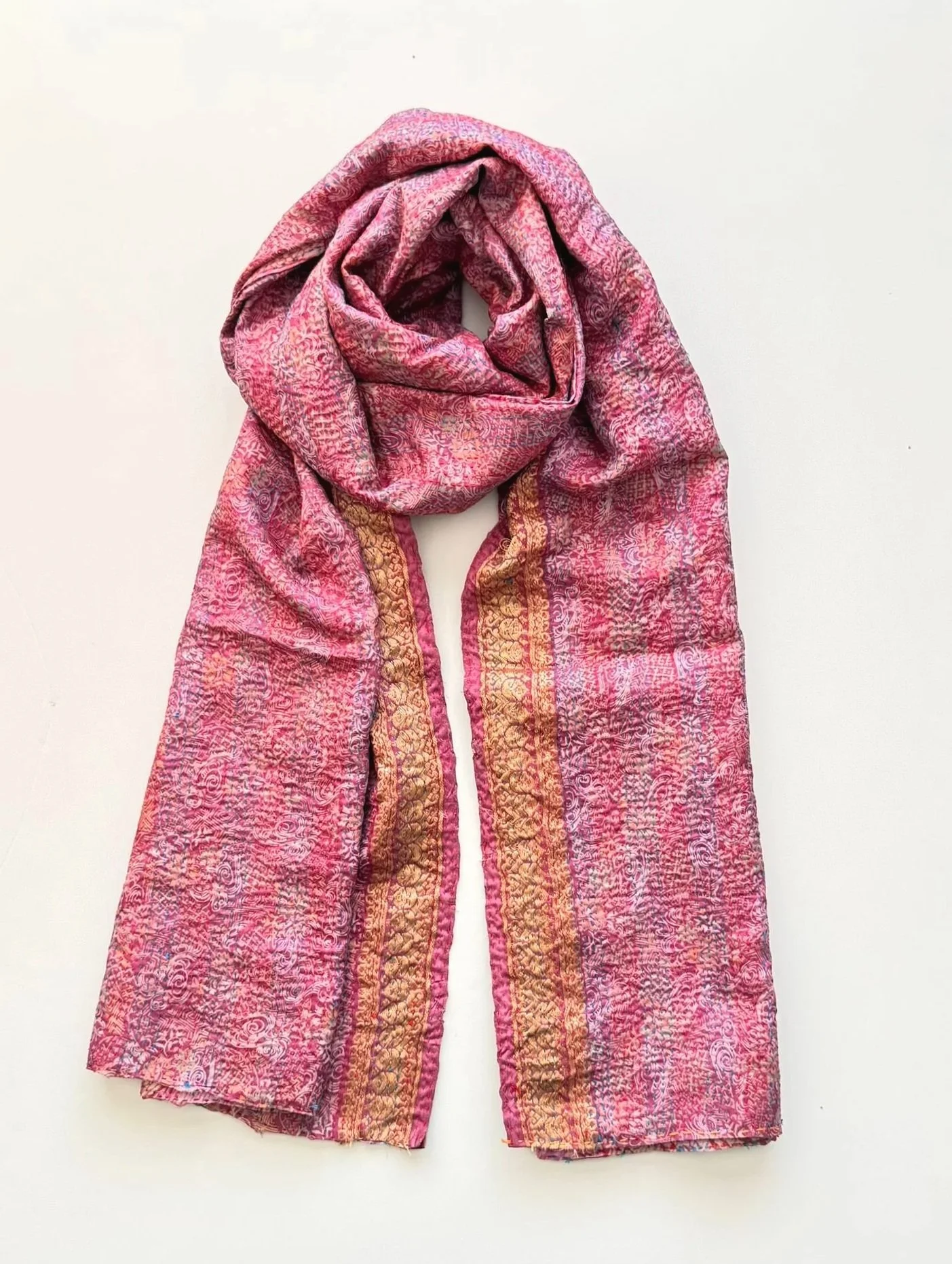 An pink silk kantha sari scarf with a gold decorative border running down the front with a floral pattern, draped in a loop elegantly on a white background.