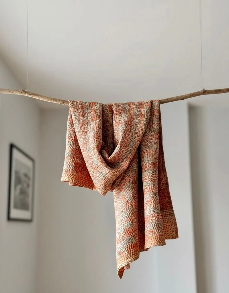 Peach recycled sari silk kantha scarf draped around a branch suspended from ceiling on a white background