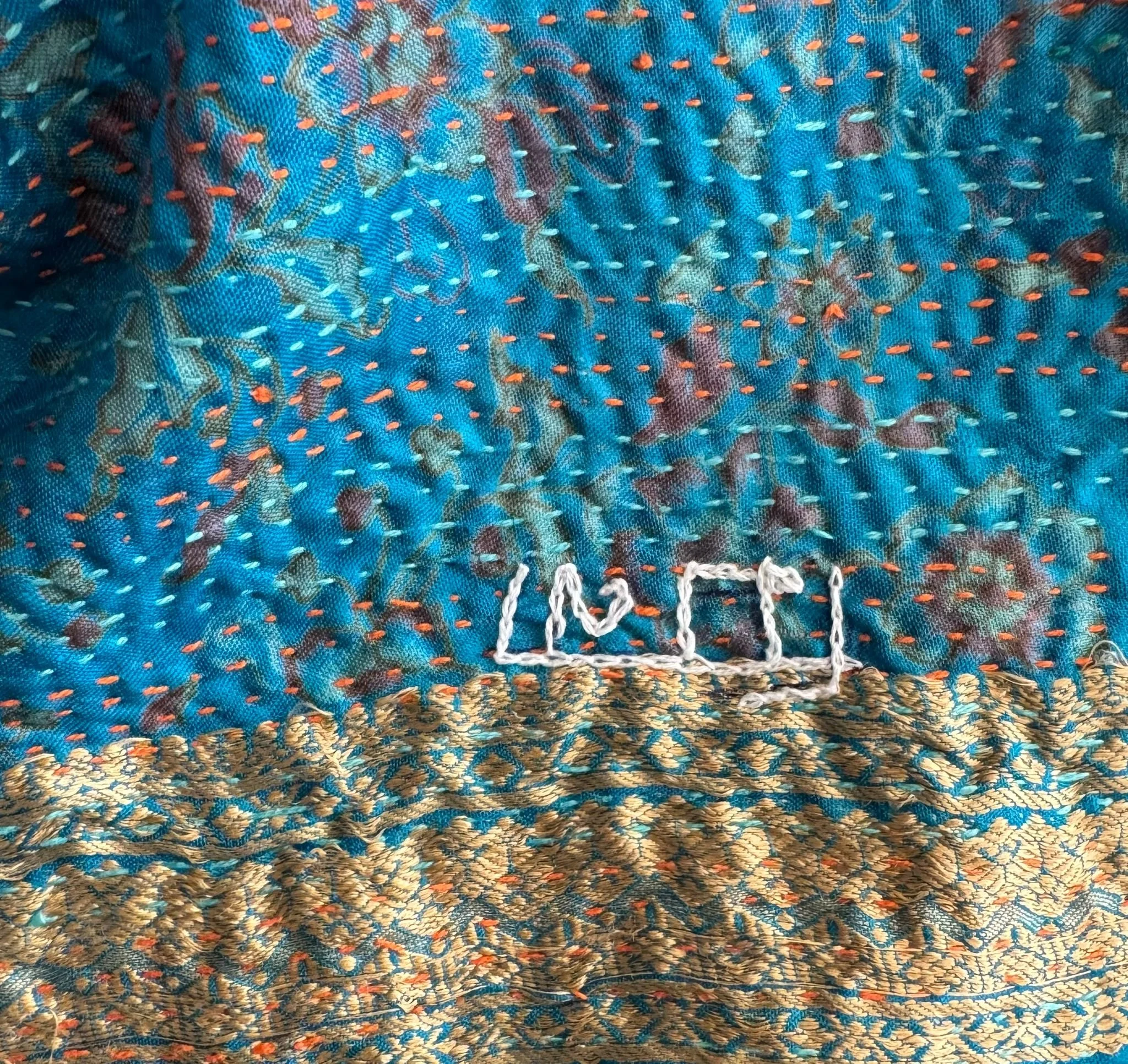 Blue and gold quilted fabric with colourful kantha stitch and name of artisan maker in Bengali