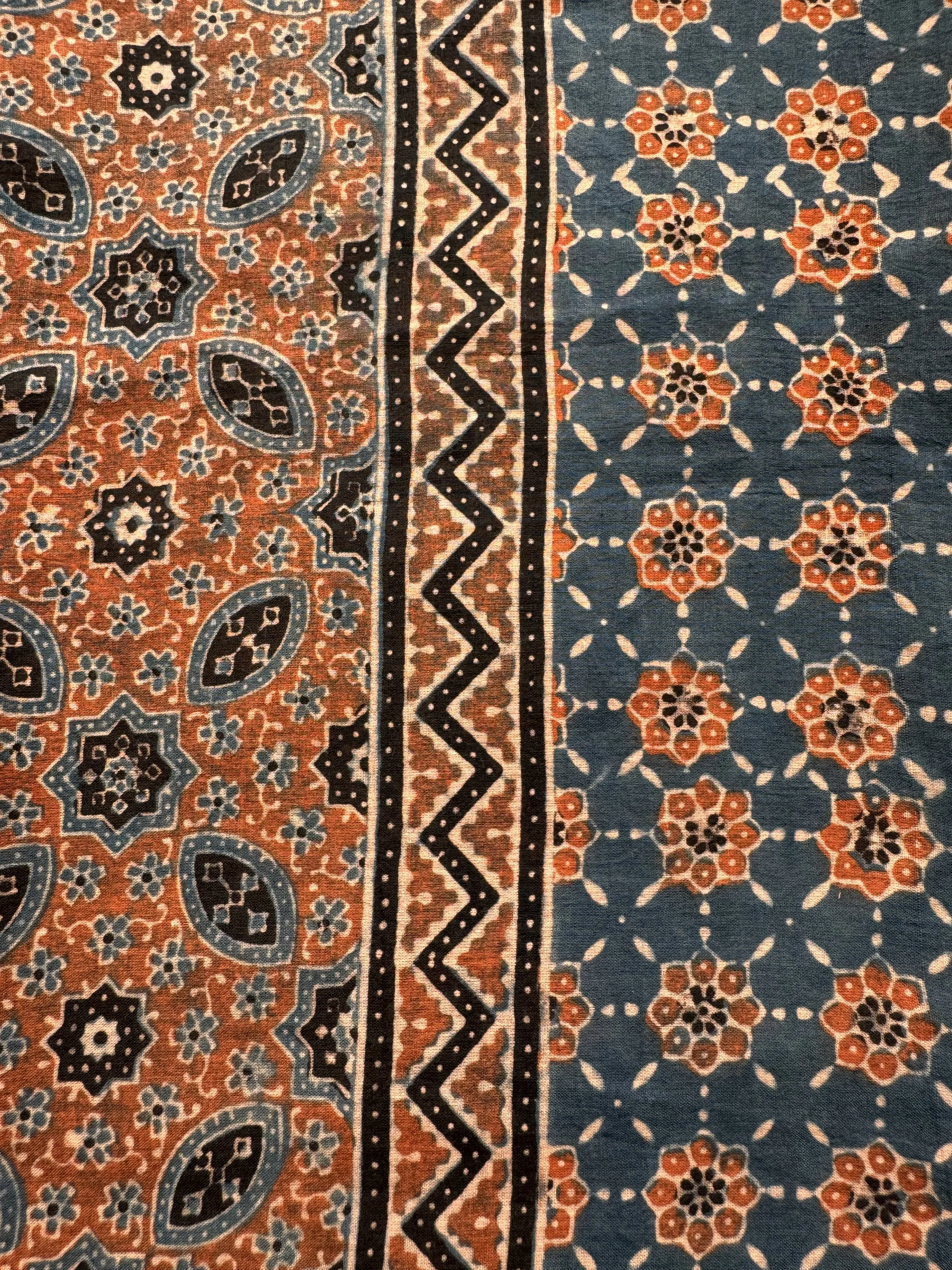 Close-up of rust red Ajrakh star and almond pattern with zigzag borders on soft cotton