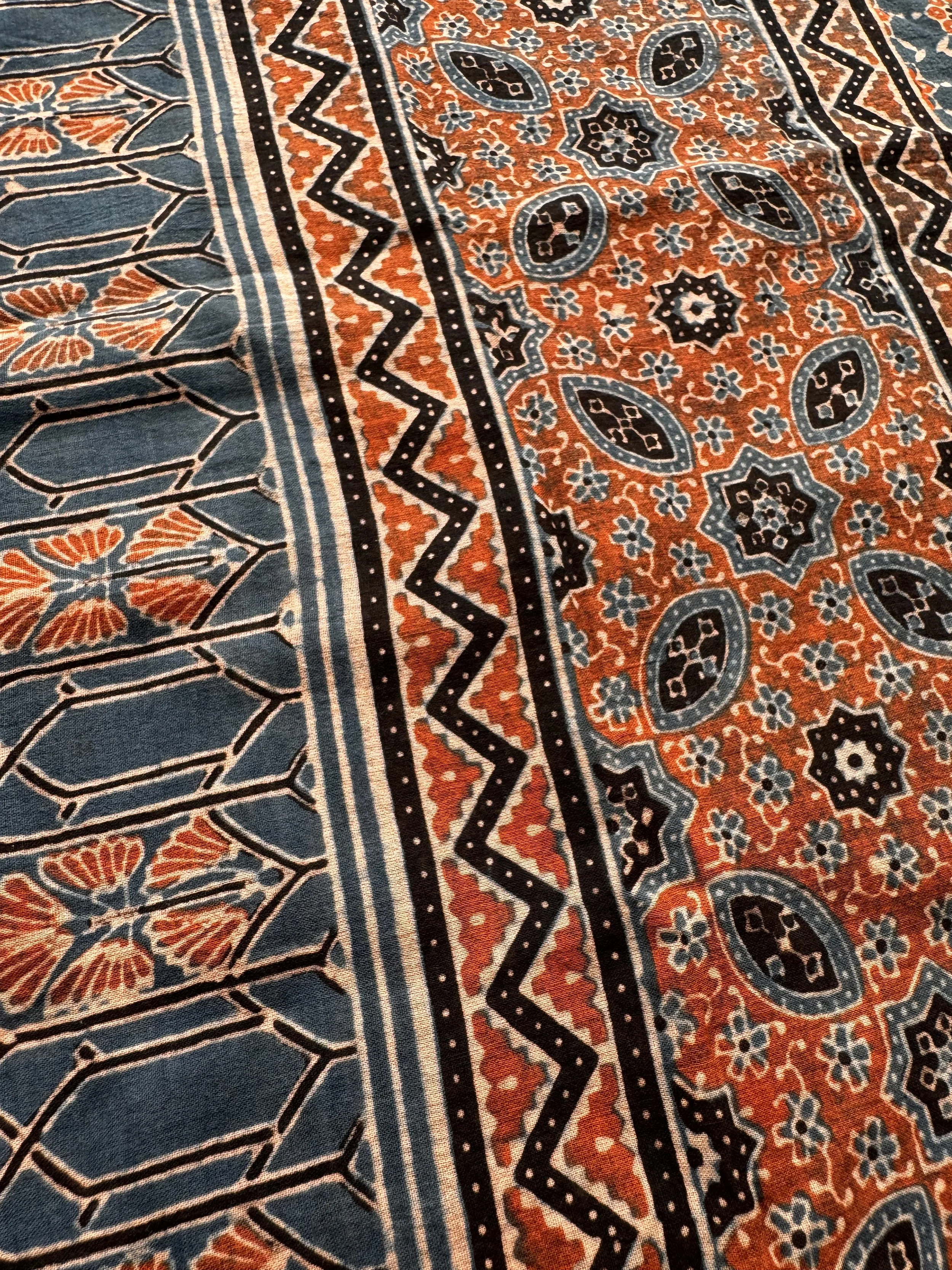 Close-up of rust red intricate Ajrakh geometric pattern with zigzag borders on soft cotton
