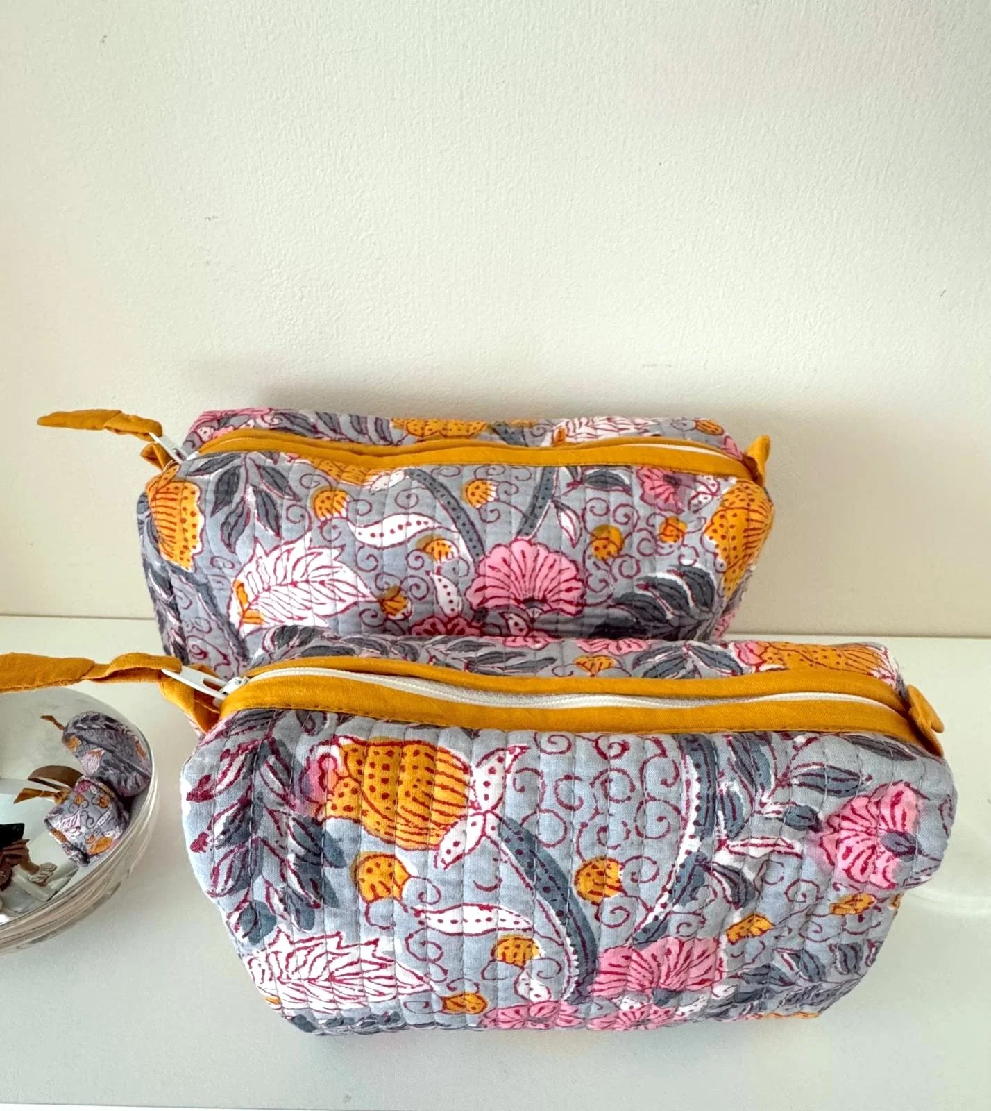 Top view of two colourful wash bags in a floral quilted cotton in shades of pink, yellow and grey, hand block printed and handmade in India for Jewelled Buddha