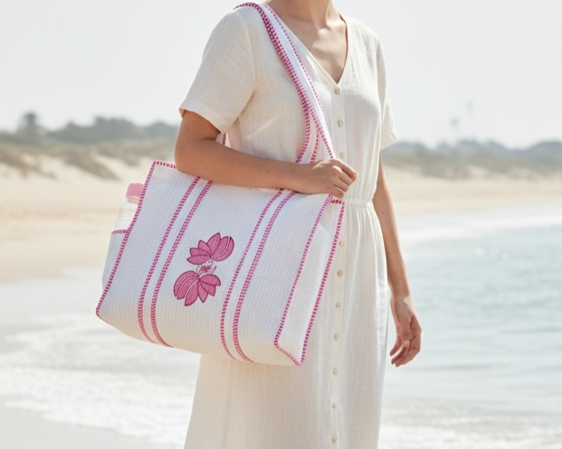 A woman walks along the beach carrying a cream and pink quilted tote bag