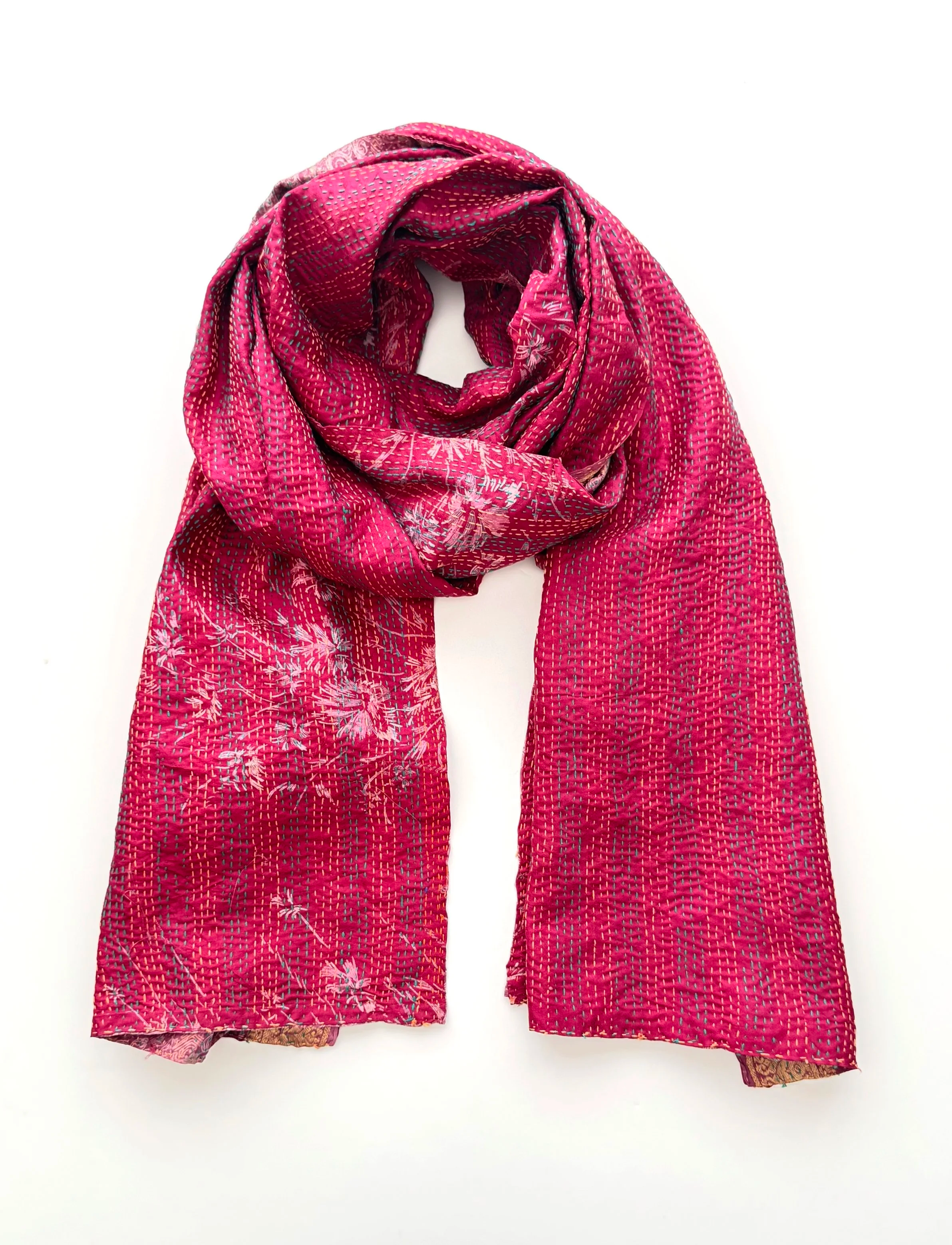 A vibrant pink scarf with white floral patterns is artistically draped against a plain white background. The fabric has a textured weave, adding depth.