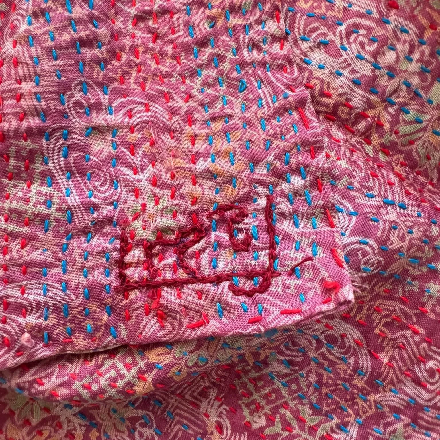 Close up hand embroidery on kantha fabric with the initials of the artisan embroidered on it in red thread.