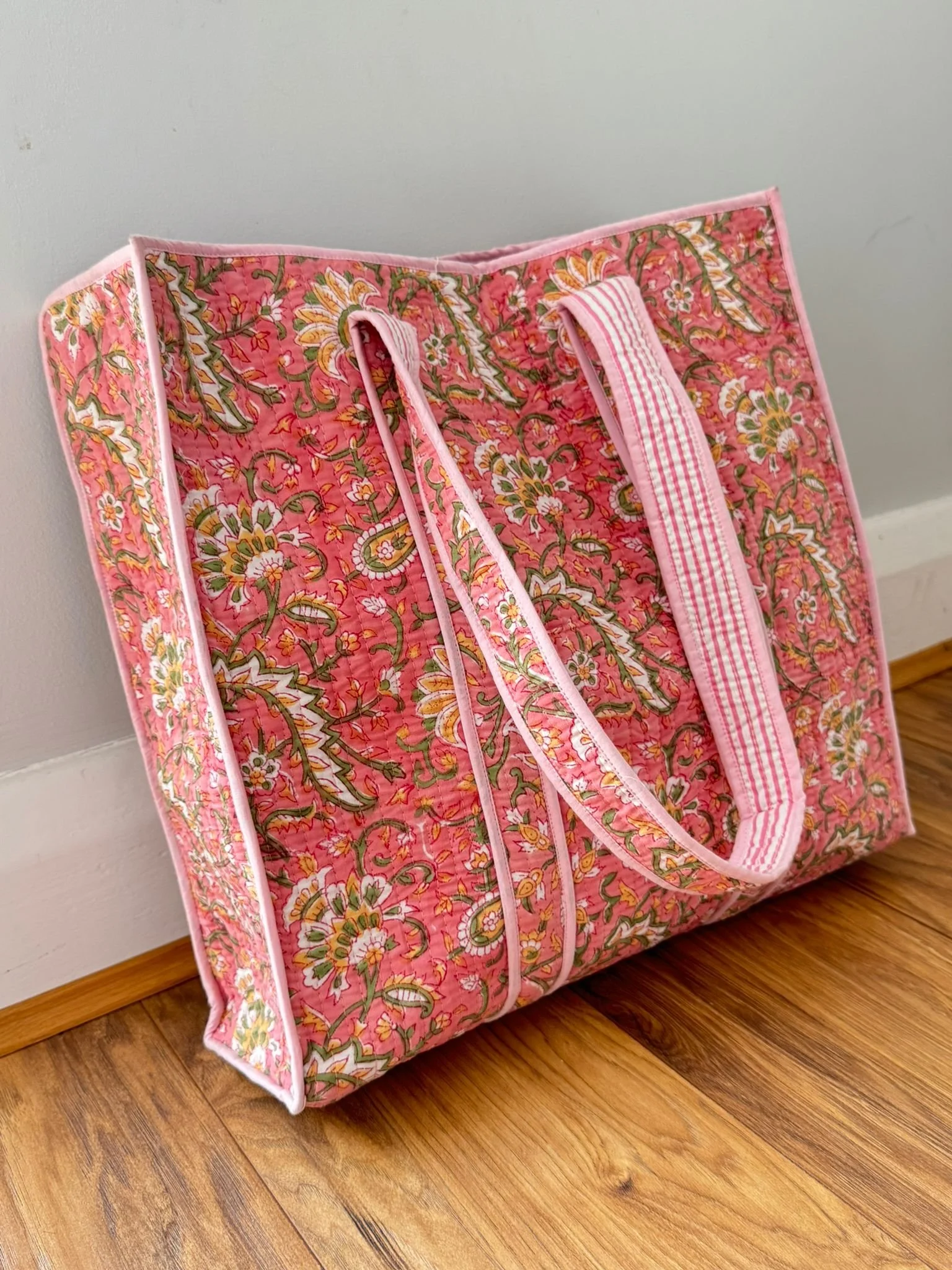 Pink block print quilted tote bag with striped shoulder straps and contrasting pink trim against a neutral background