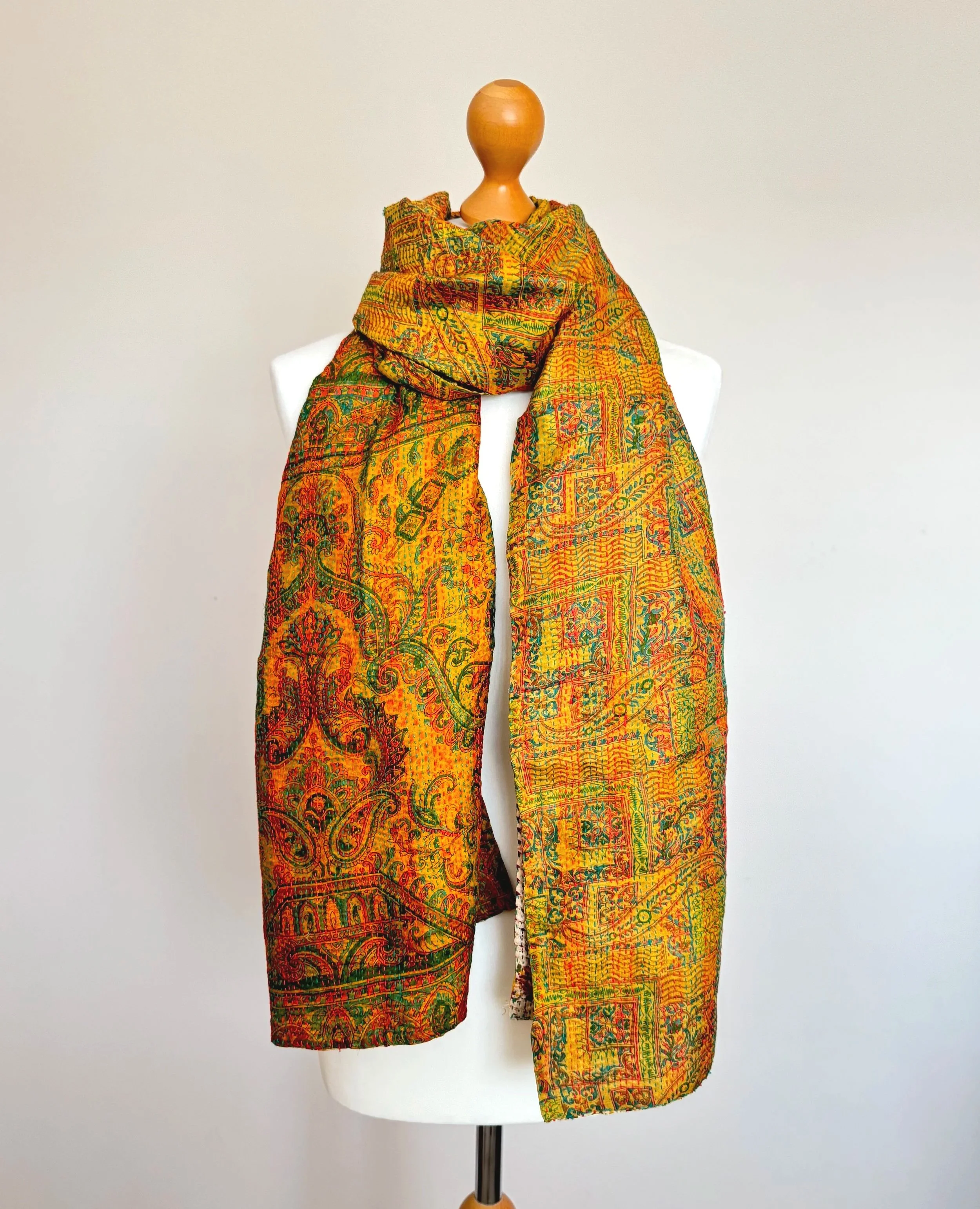 A yellow and green richly textured scarf with a floral pattern elegantly draped over a mannequin against a white background