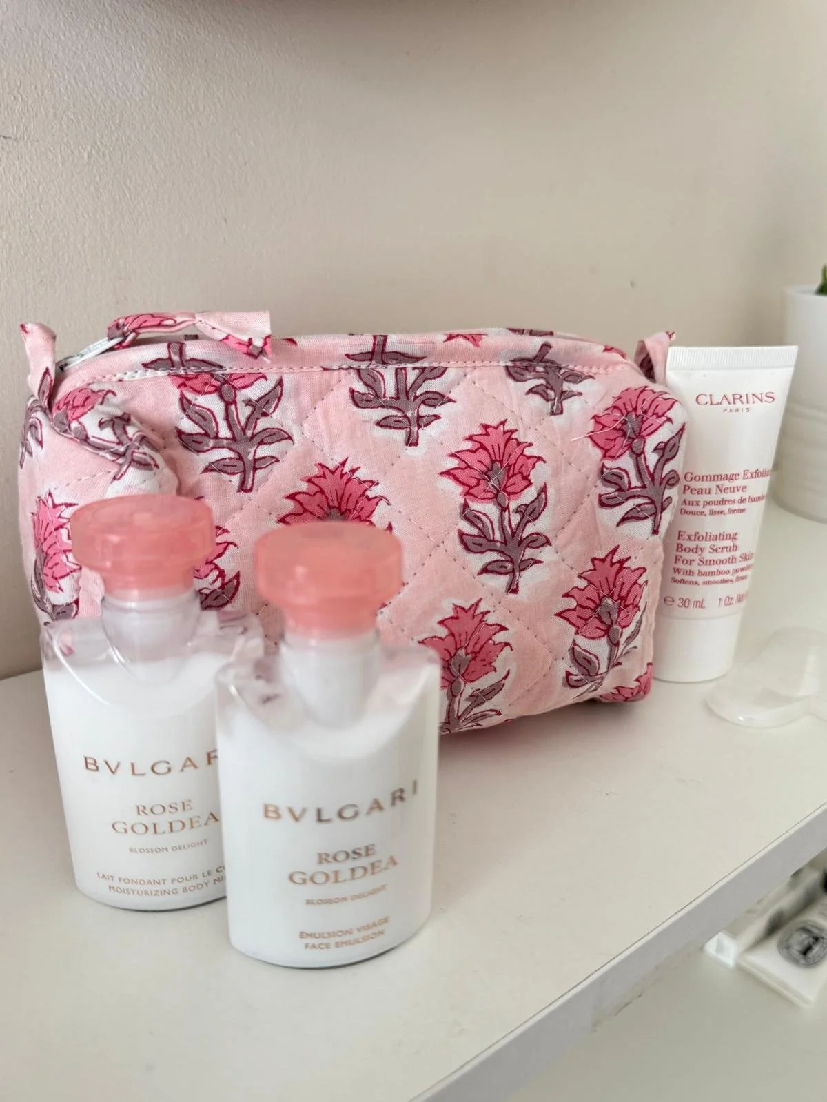 A pink quilted cotton wash bag with hand block print design resting on a white bedroom shelf surrounded by toiletries