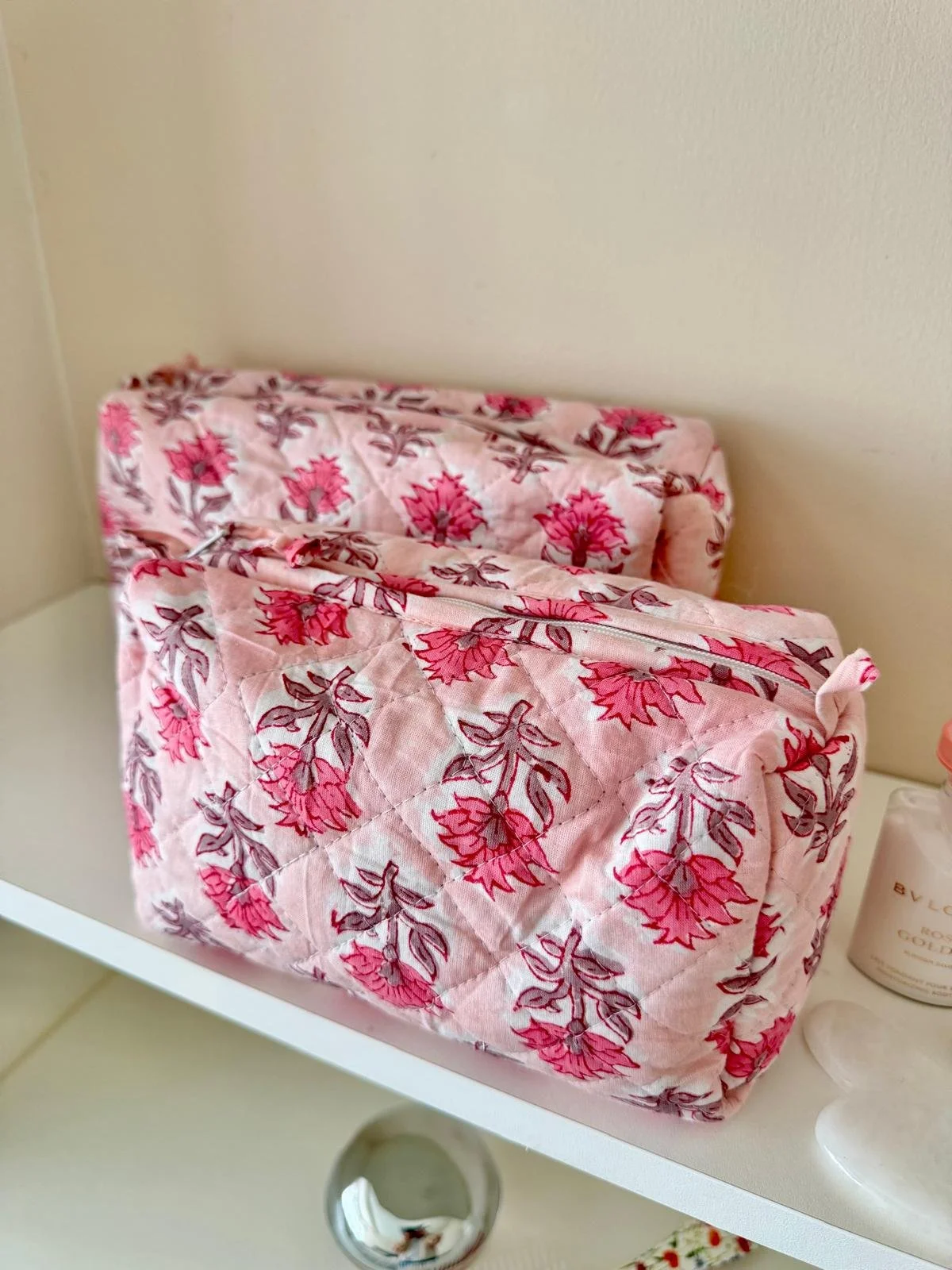 Two Pink floral block print quilted cotton wash bag with zip resting on a white shelf