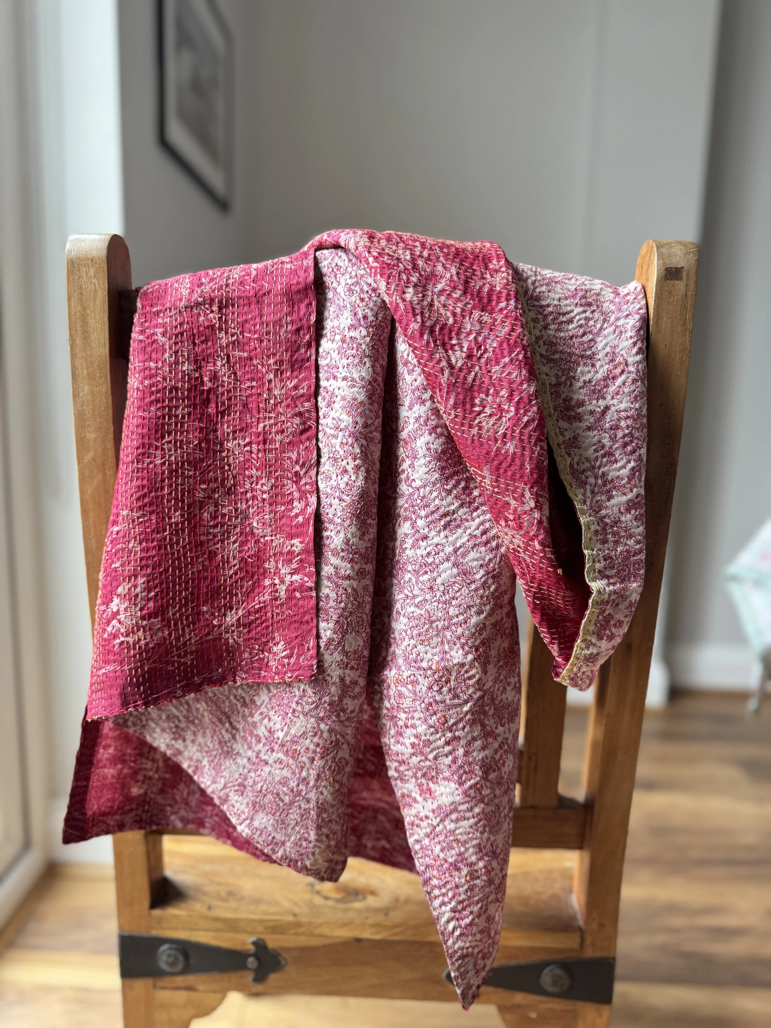 A colourful pink silk scarf with floral print draped over a wooden Jali style chair, the scarf has the name of the artisan embroidered in red and features hand embroidered kantha stitch all over