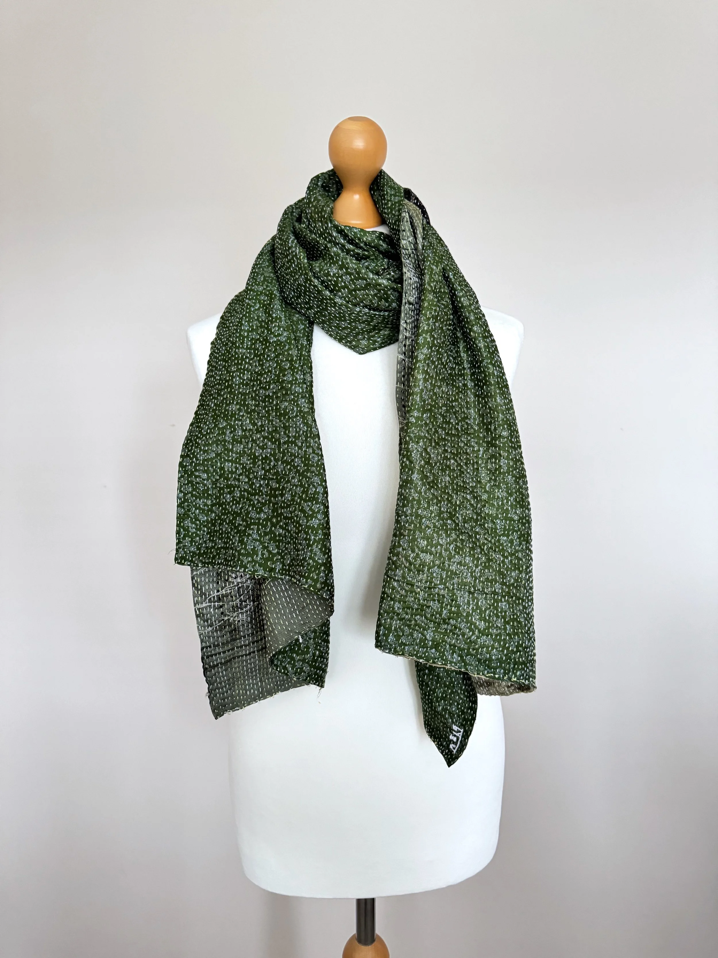 Dark green silk scarf draped around a white mannequin, handmade from recycled sari silk and hand embroidered with kantha stitch.