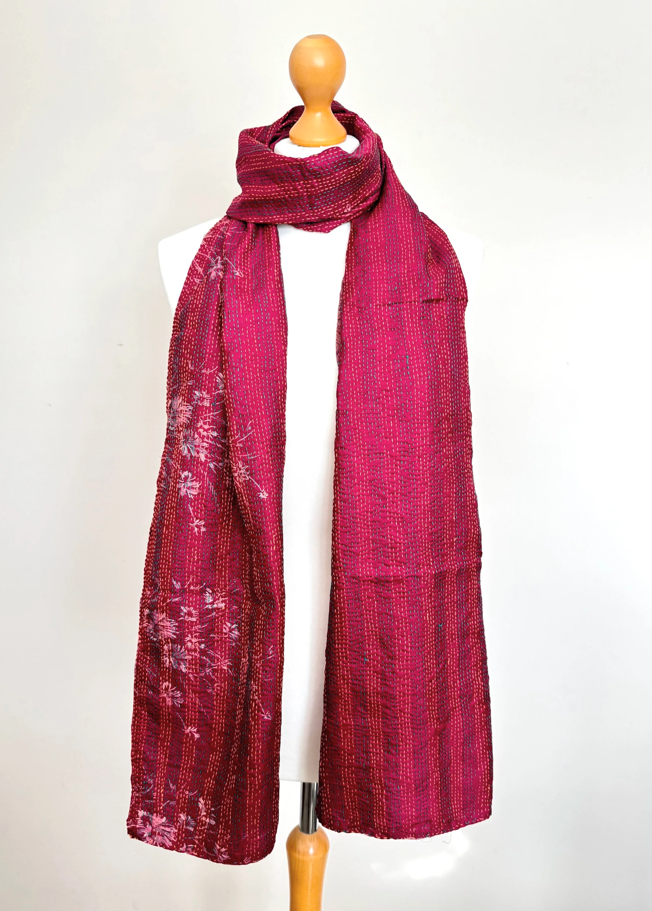 A vibrant magenta pink scarf with subtle silver floralpatterns draped over a white mannequin, set against a plain background. The scarf conveys elegance.