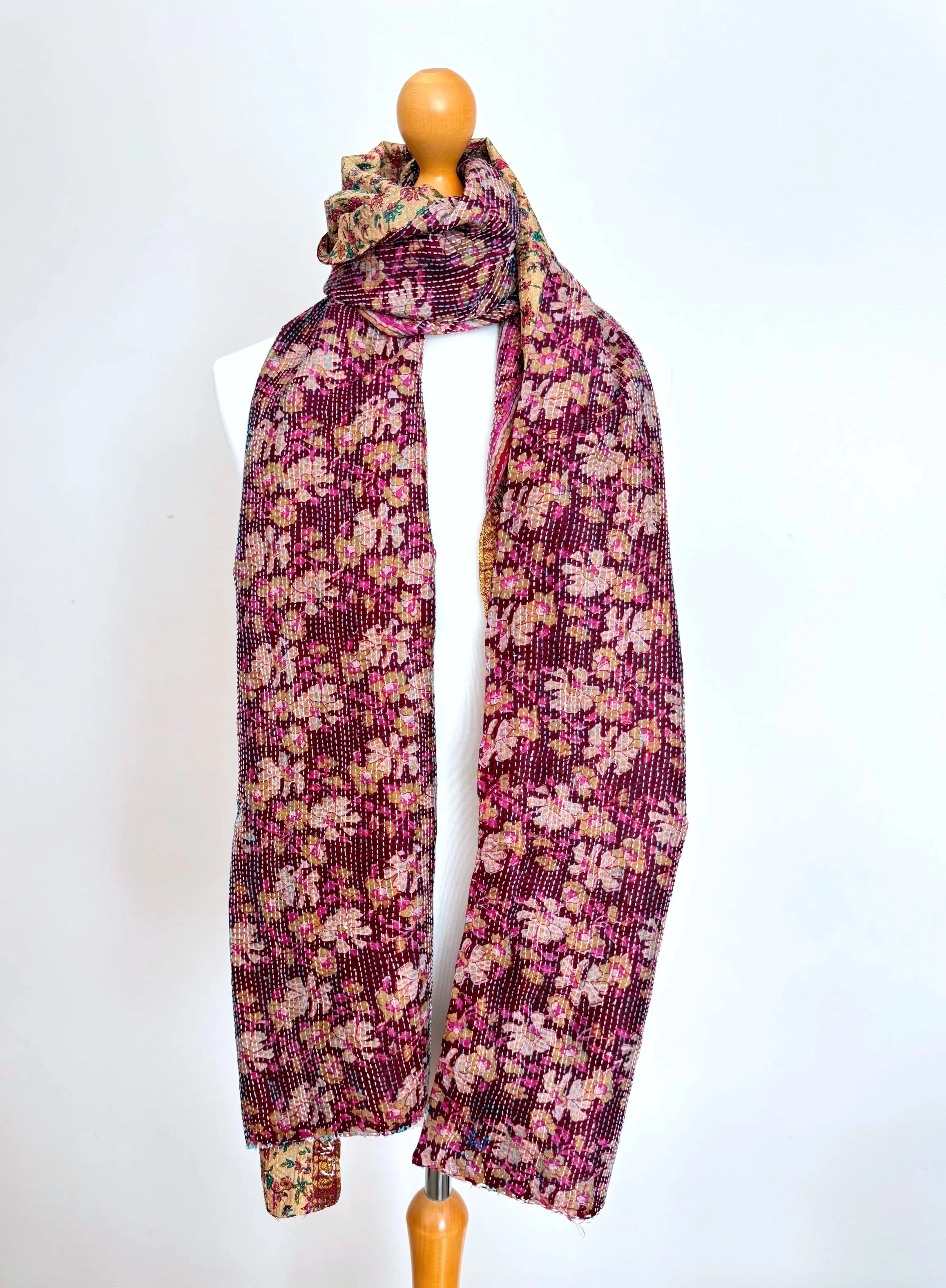 A vibrant scarf with a floral pattern in deep plum colours draped over a mannequin in a neutral background.
