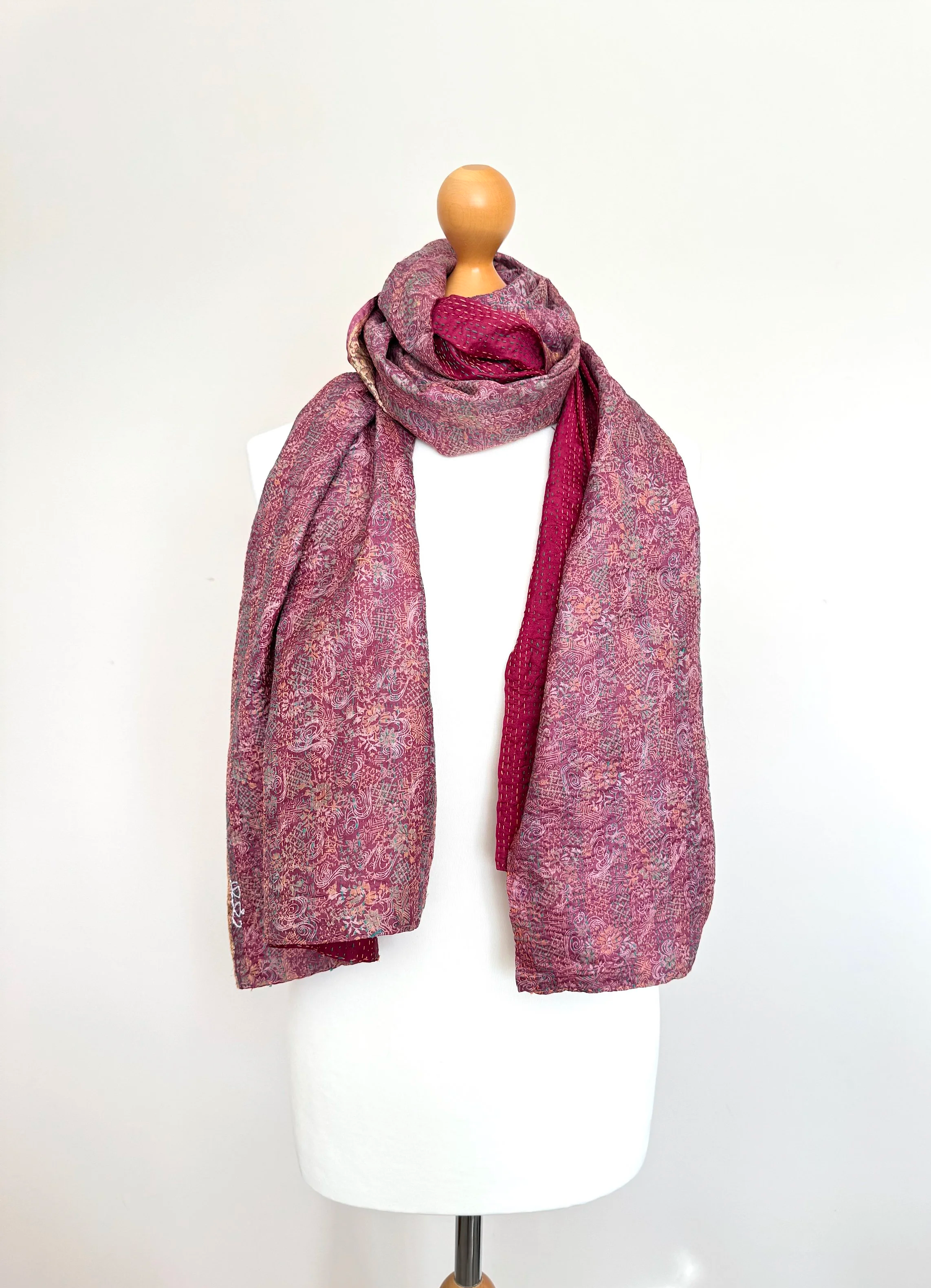 A mannequin displays a textured, pink-and-red scarf draped stylishly around its neck. The background is plain white, highlighting the scarf's pattern