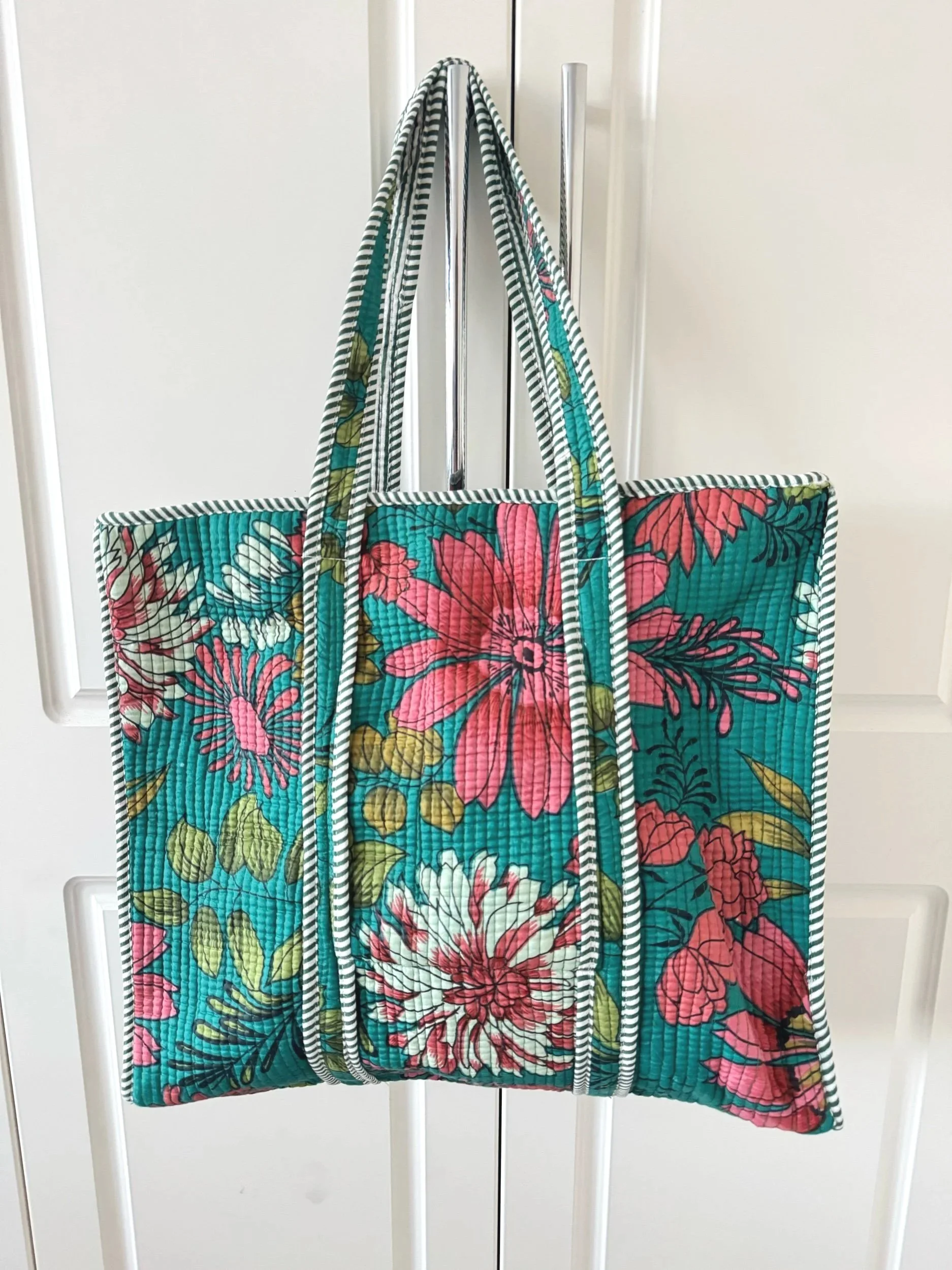 Handmade blooming flower print teal quilted cotton tote bag with pink and white florwers on a teal fabric, hanging from a wardrobe handle.
