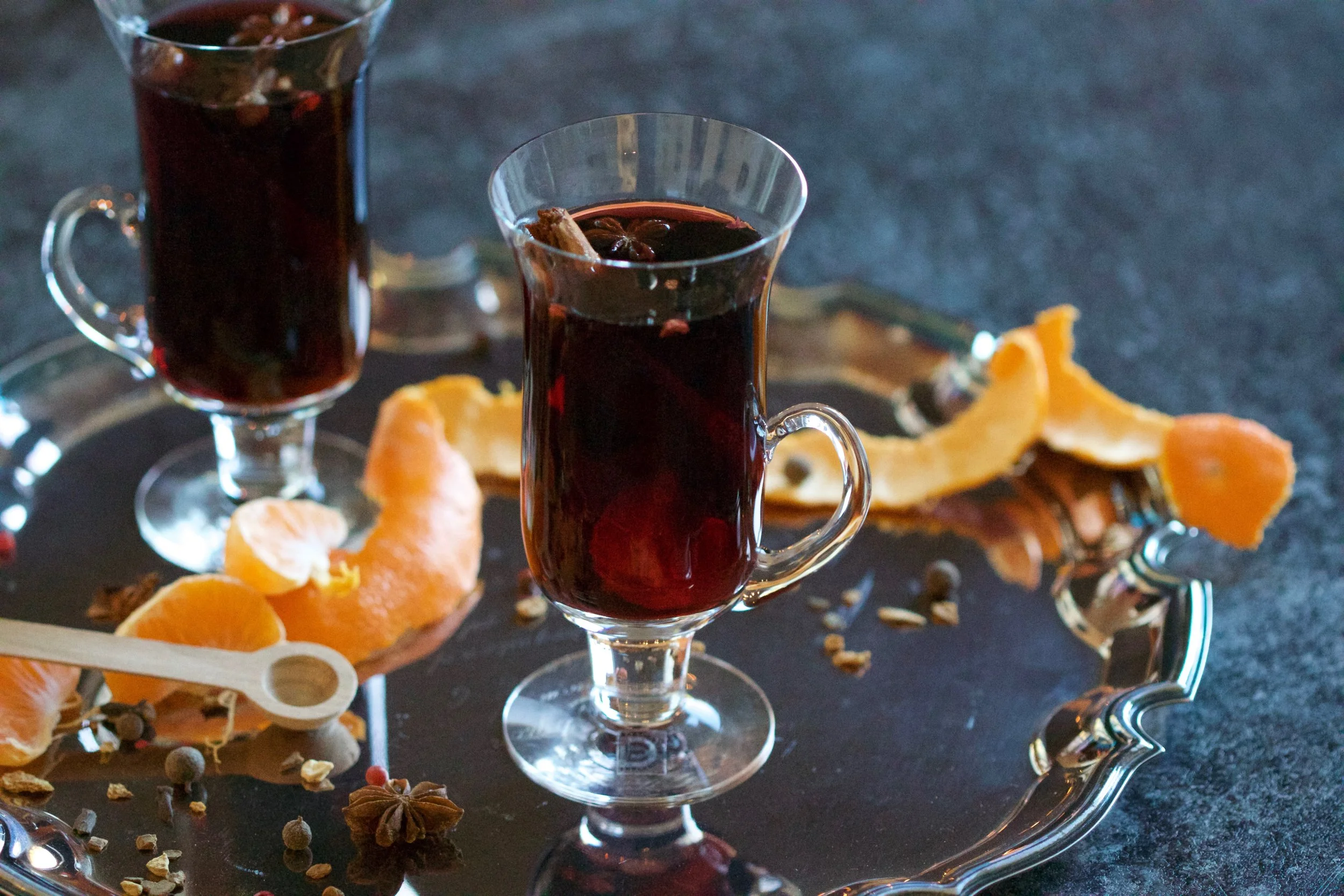Two glasses of mulled wine on a silver serving tray with orange rinds