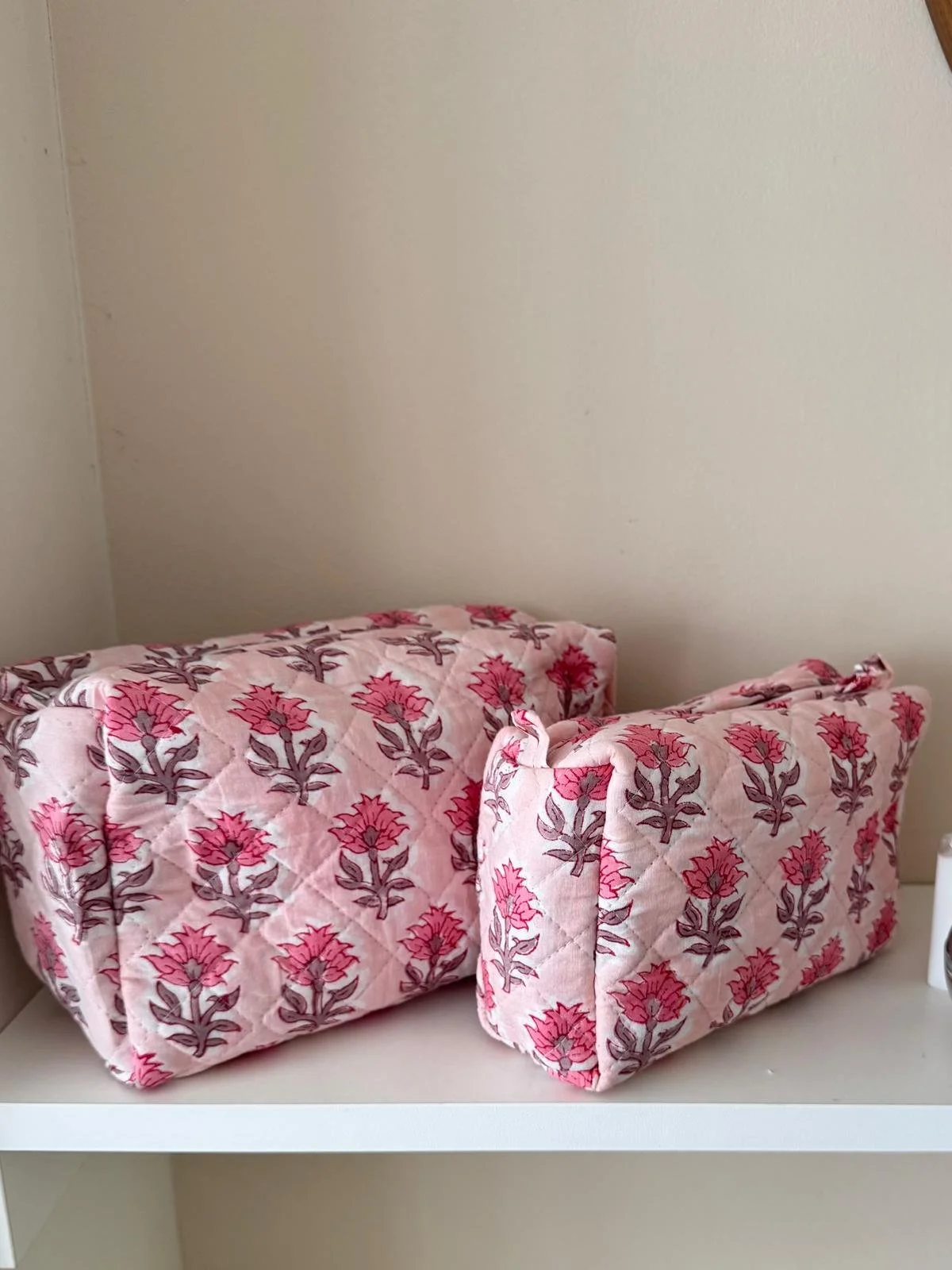 A large and medium sized blush pink floral wash bag set handmade from quilted cotton resting on a white shelf