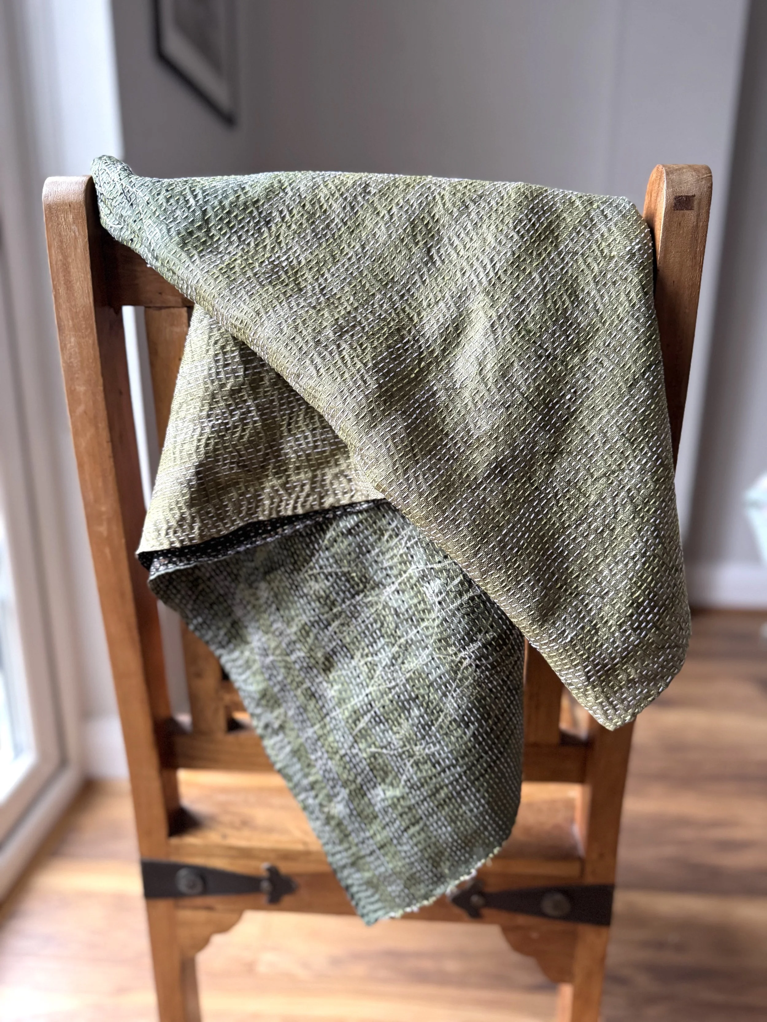 Reversible green recycled sari silk scarf in shades of olive draped over a wooden Jali style chair
