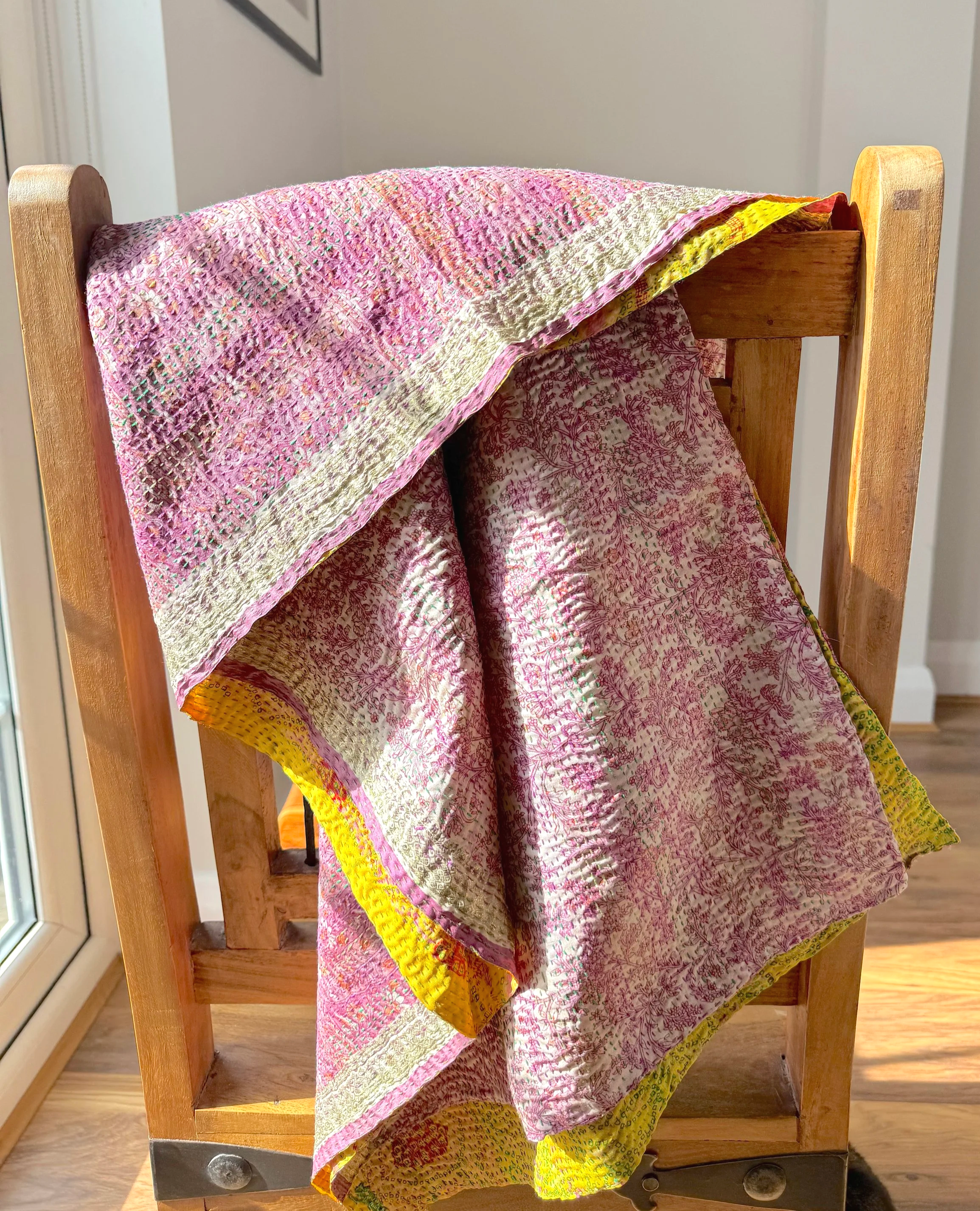 A colourful pink kantha sari scarf draped over a wooden Jali style chair, the scarf has the name of the artisan embroidLong red in red and features hand embroidered kantha stitch all over