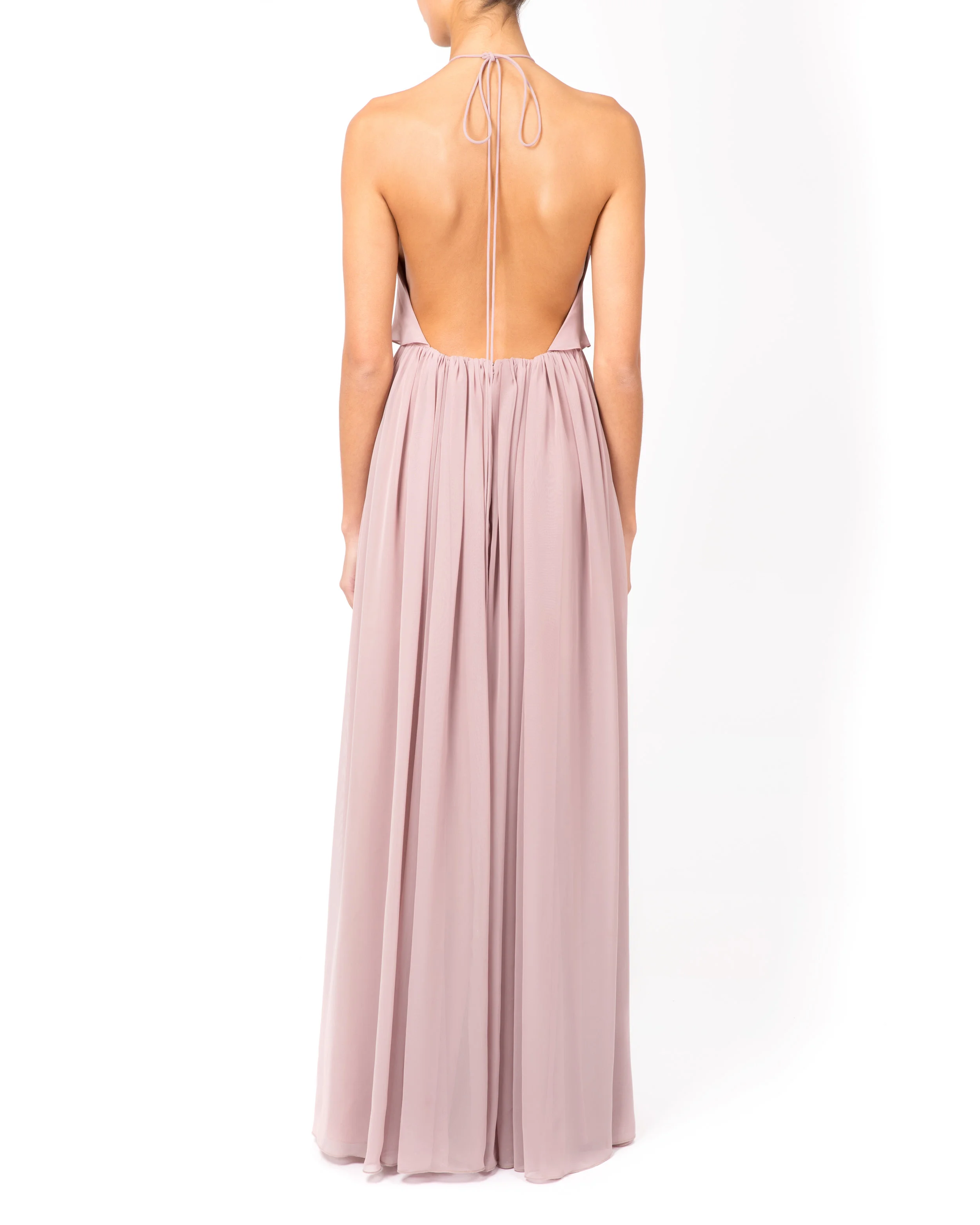 Woman wearing a backless halterneck dress in a dusky pink colour with a bow tied at the top.